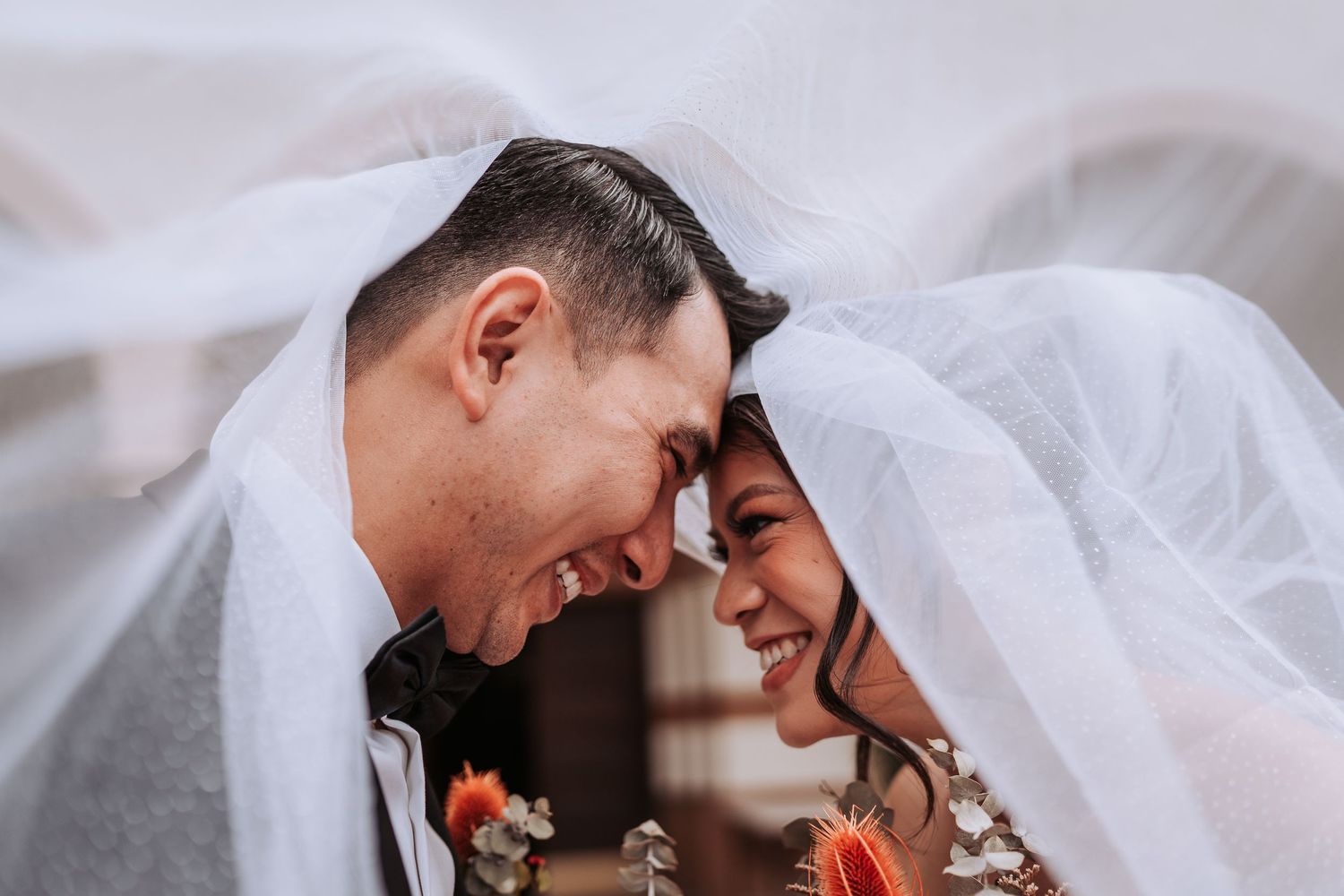 Newlyweds share an intimate moment under a flowing white veil during their wedding ceremony.