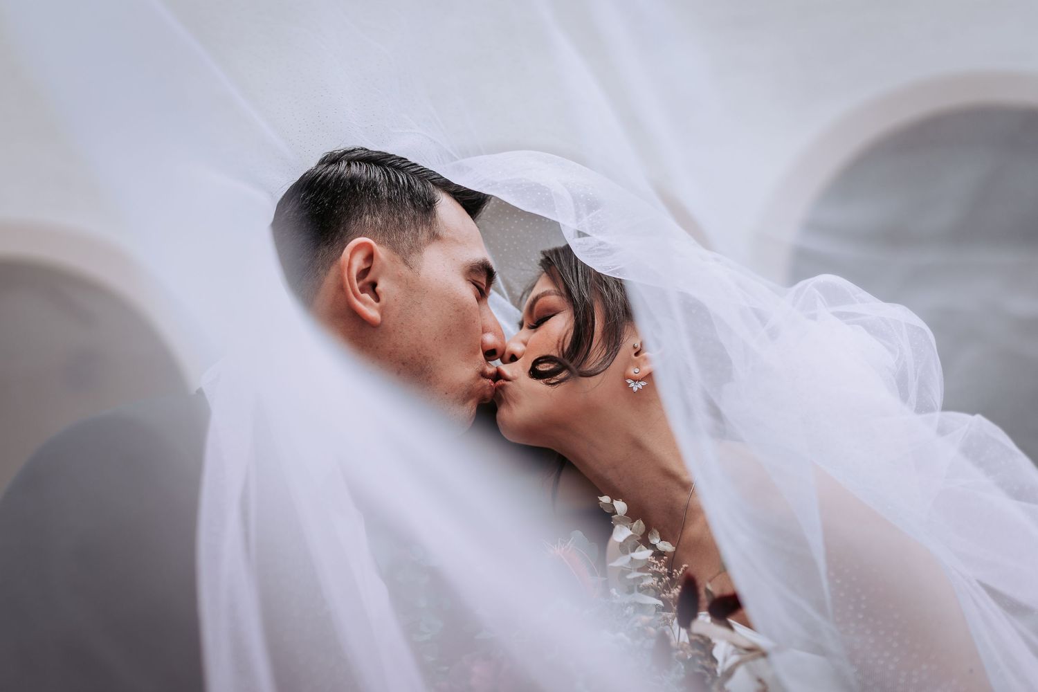 Close-up wedding photo showing a tender moment between newlyweds beneath a delicate white veil.