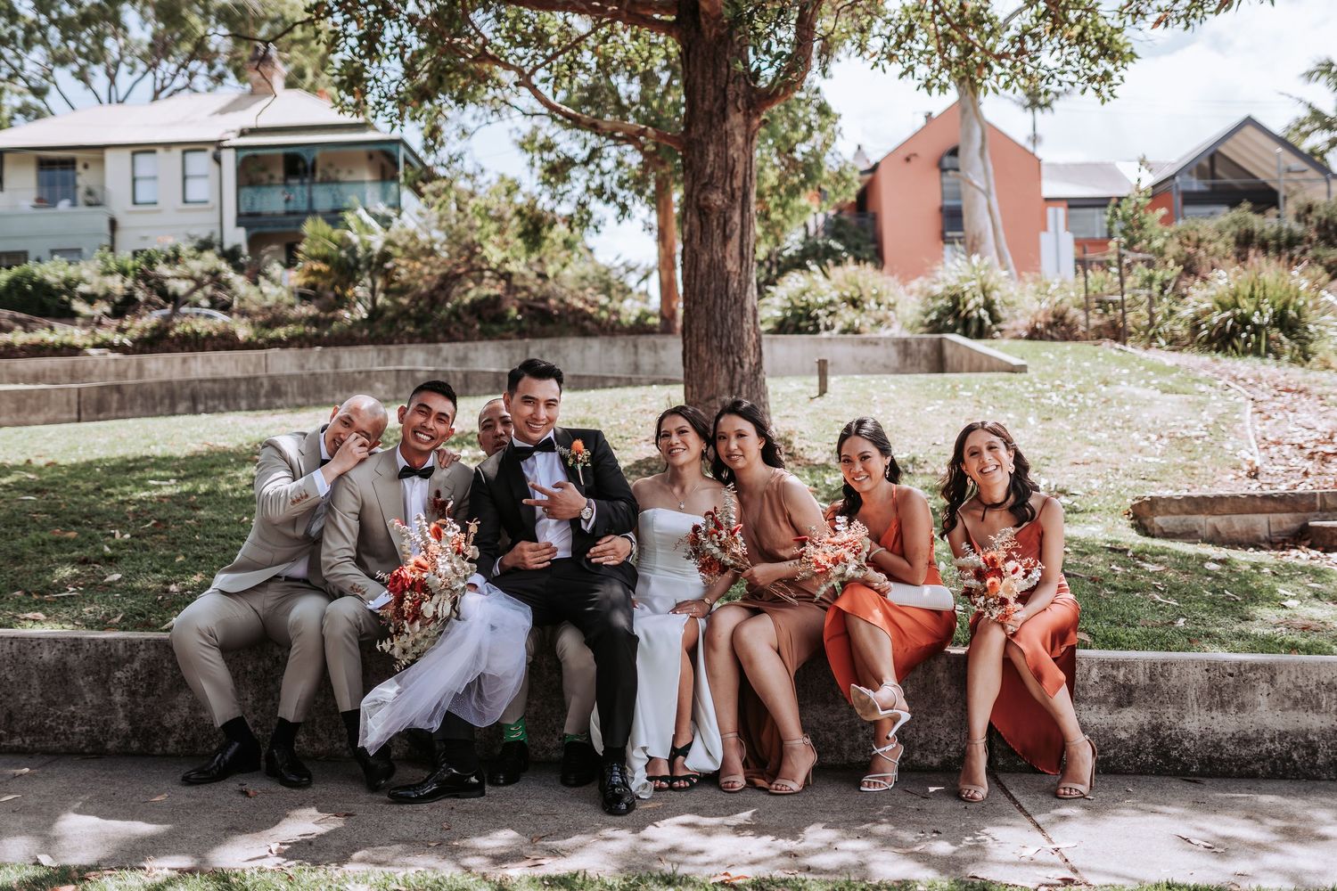 Bridesmaids in coral and peach dresses celebrate joyfully at outdoor wedding venue.