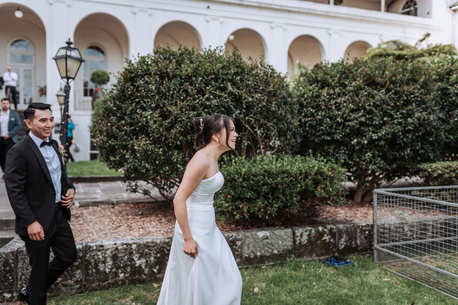 Bride in white dress reaches out to pet a llama in an outdoor garden setting.