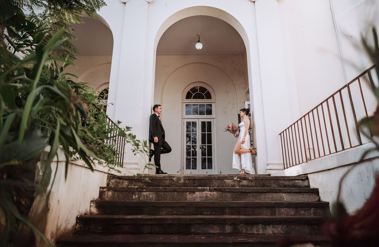 Two people stand on opposite ends of grand stone steps leading to an arched entrance of a classic white building.