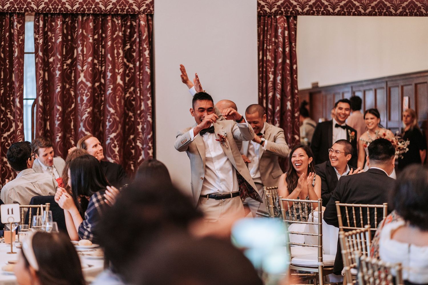 Wedding reception speech being given in an elegant ballroom with damask curtains.