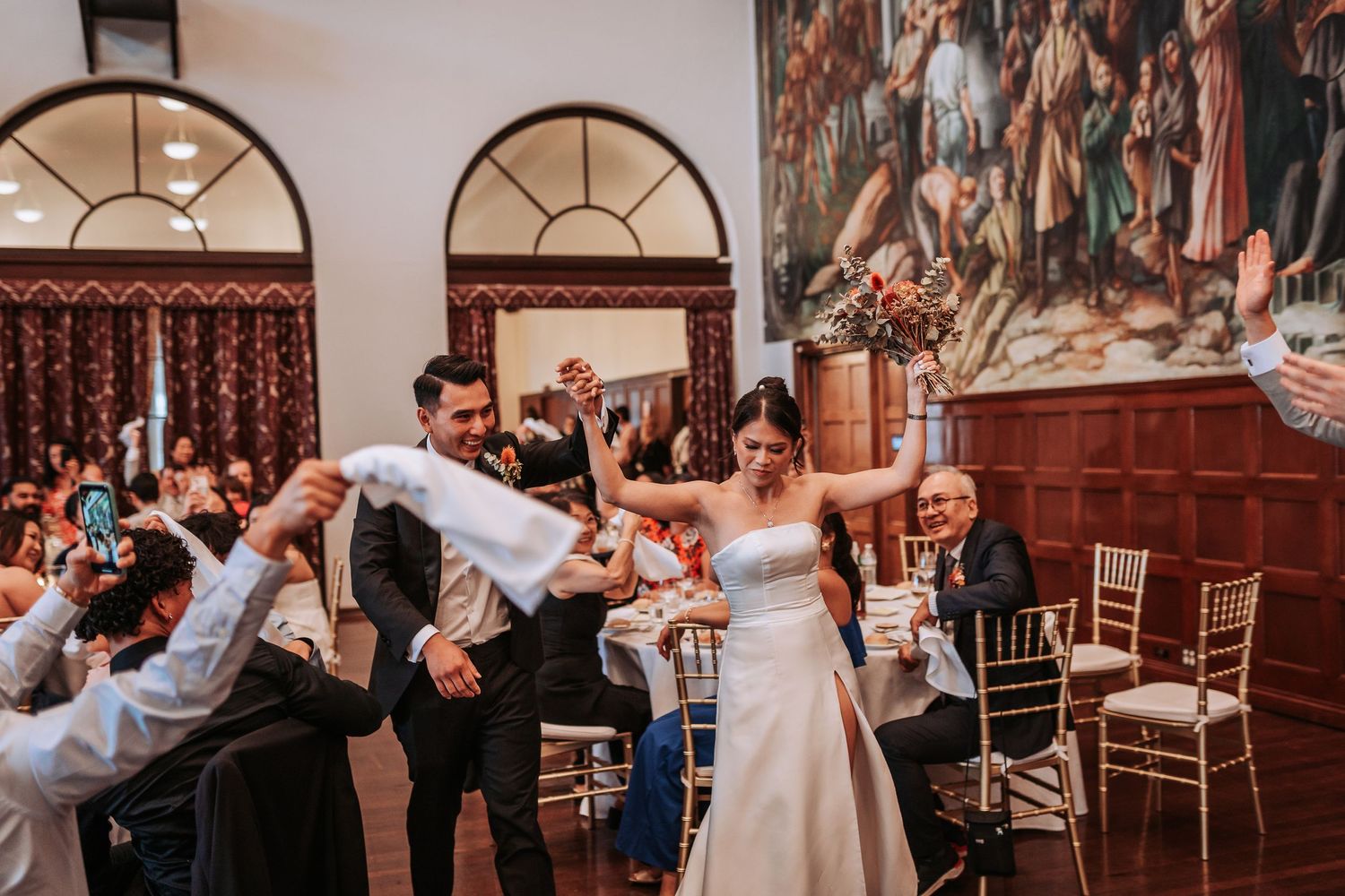 Wedding celebration with guests lifting couple during reception in an ornate ballroom.