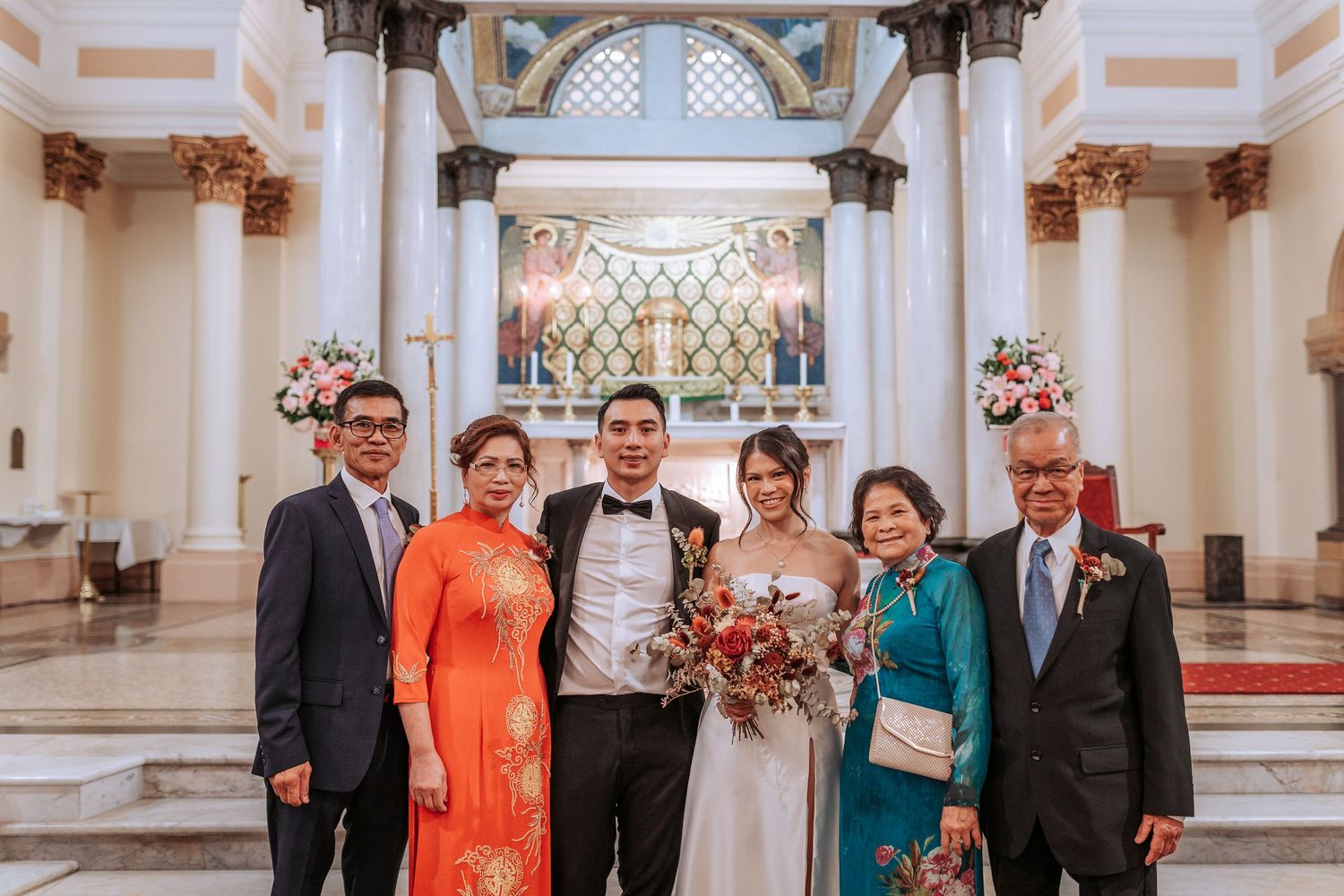 Wedding party poses for formal photo at church altar with elegant floral decorations.
