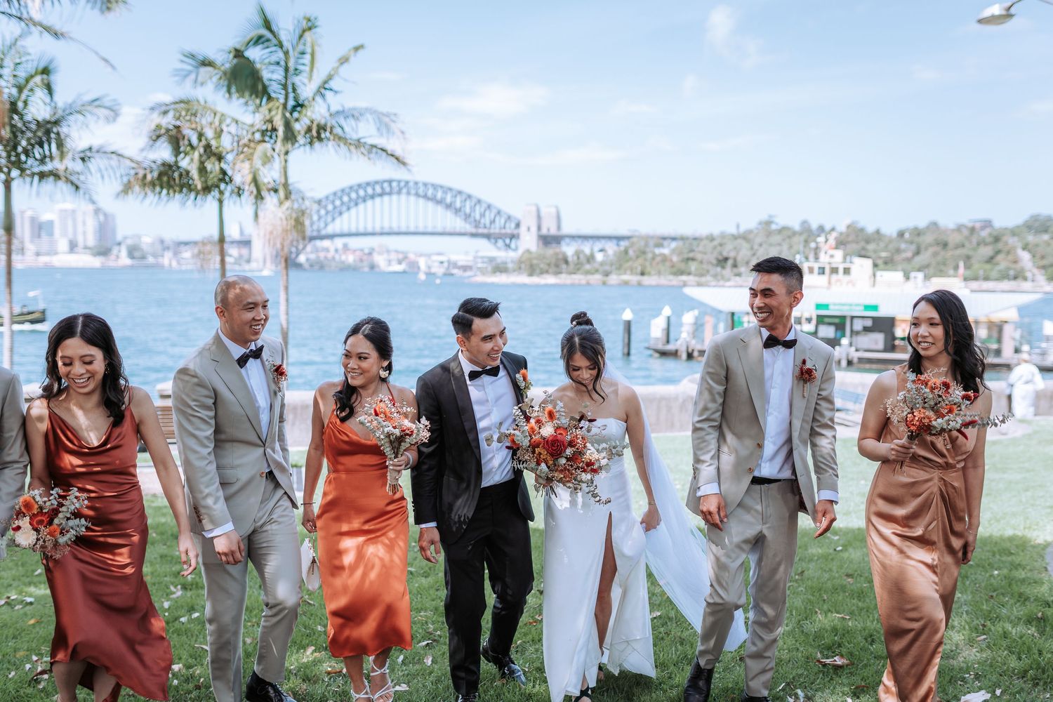 Wedding party walks on lawn with Sydney Harbour Bridge and palm trees in background.