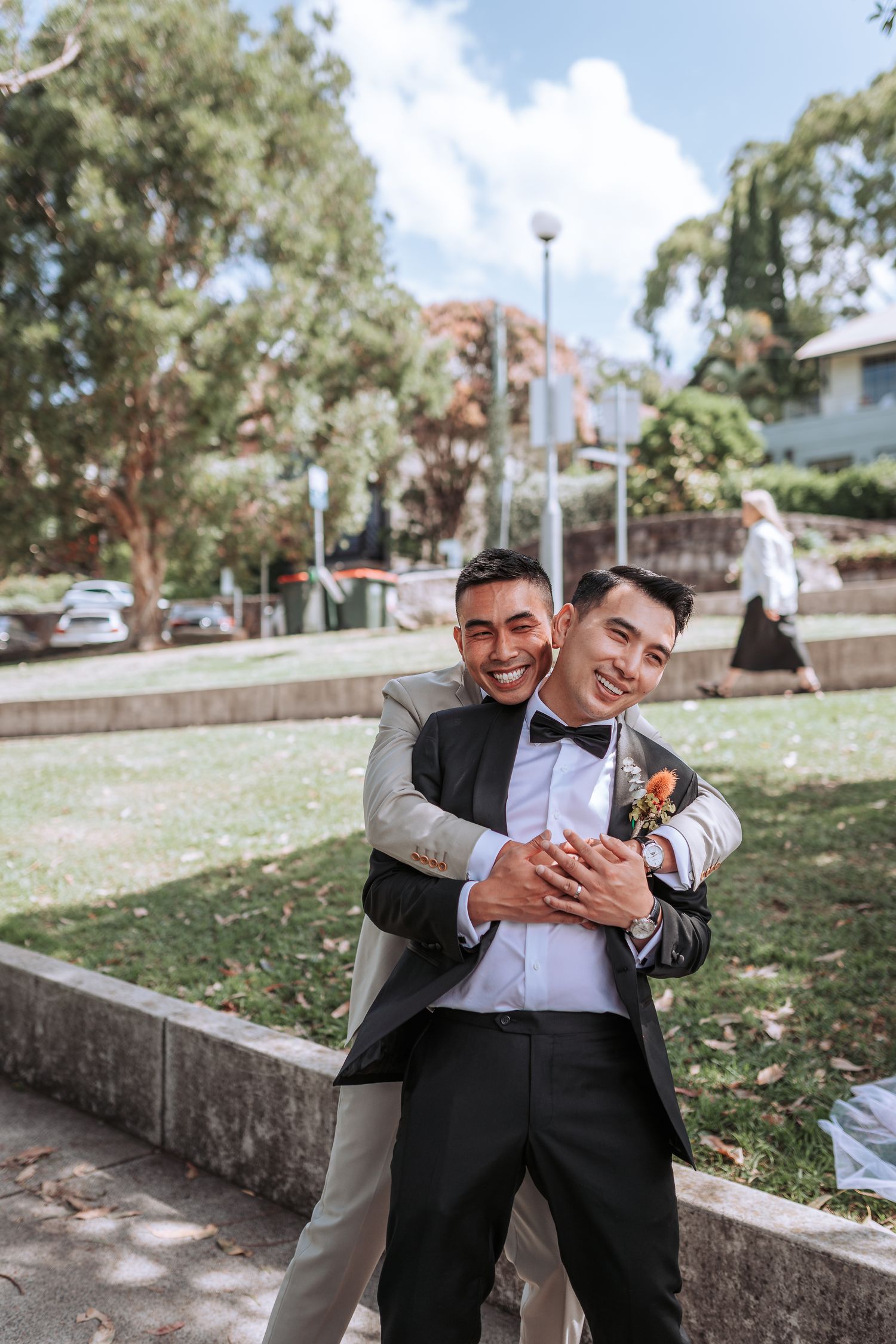 Two groomsmen share playful moment outdoors in formal wedding attire.