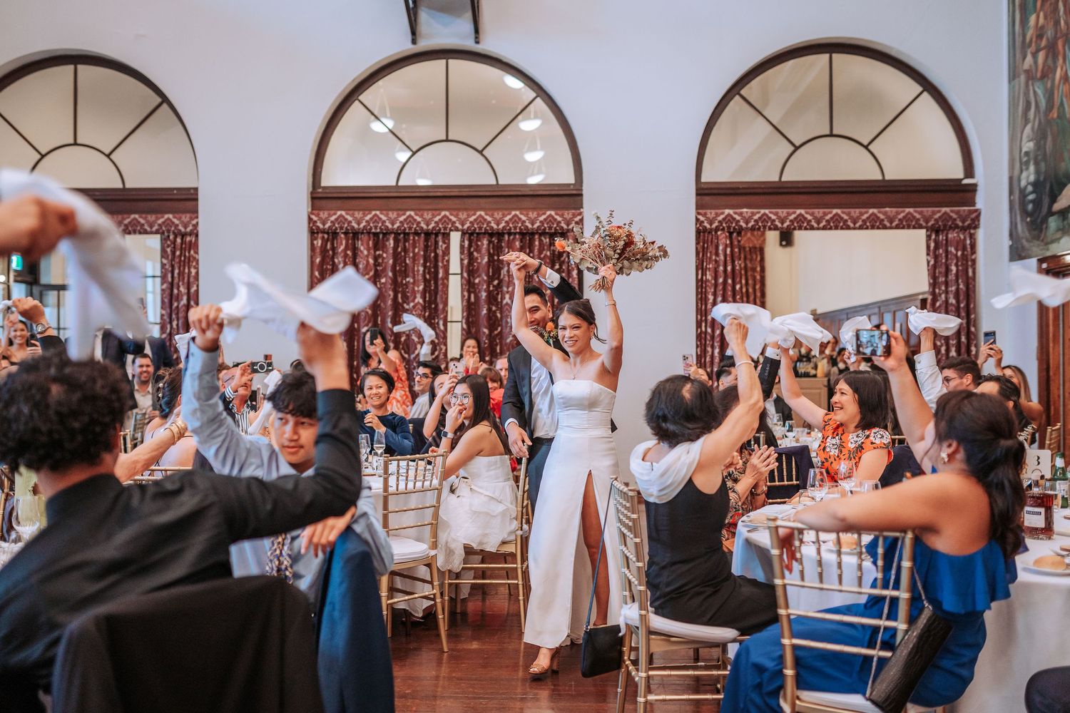 Wedding celebration with guests dancing and waving napkins in an elegant ballroom.