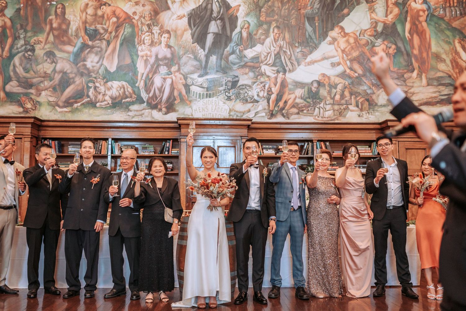 Wedding party lineup poses together in front of an ornate mural in an elegant venue.