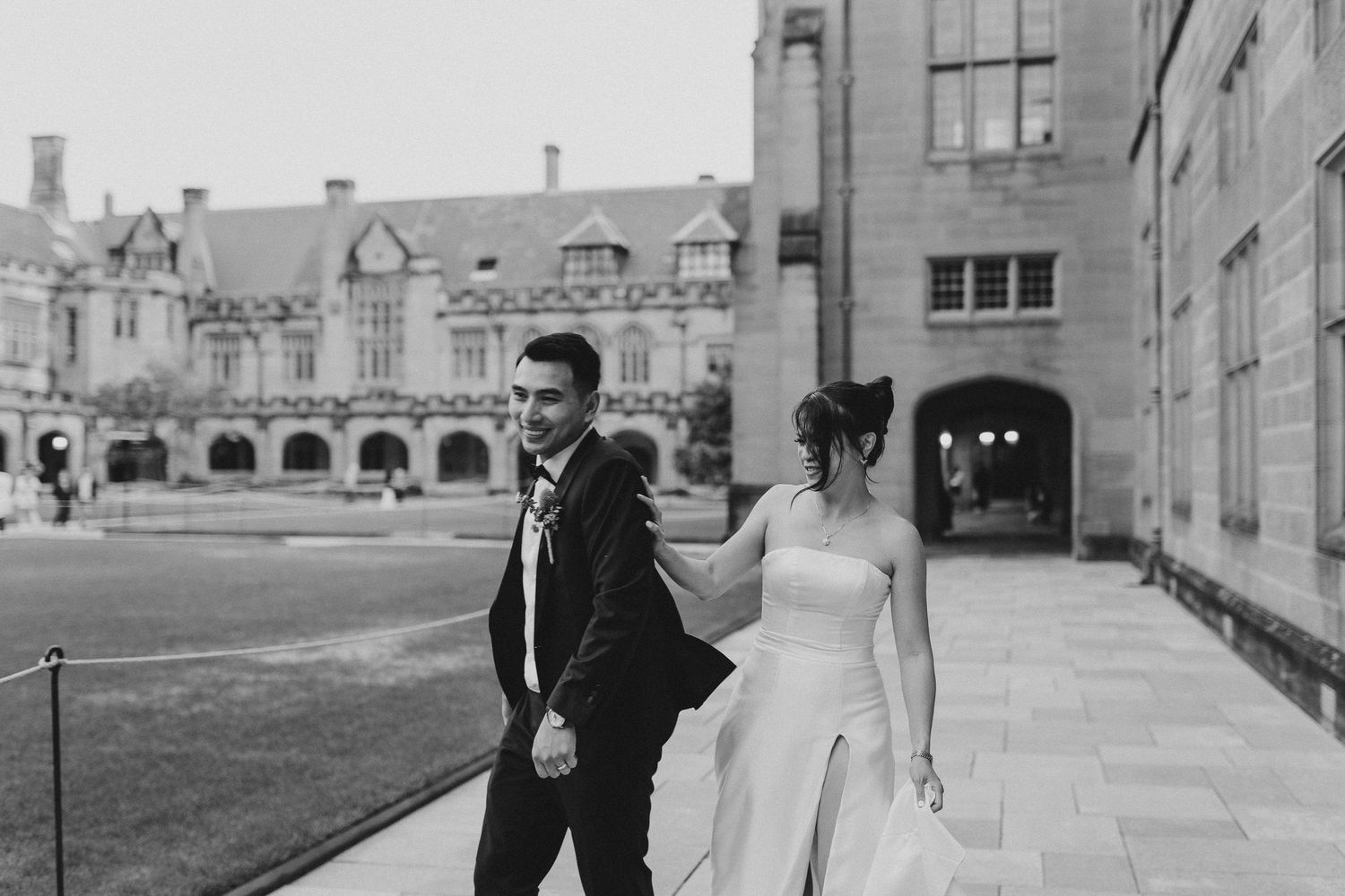 Black and white photo of a couple walking outside a historic gothic architecture building.