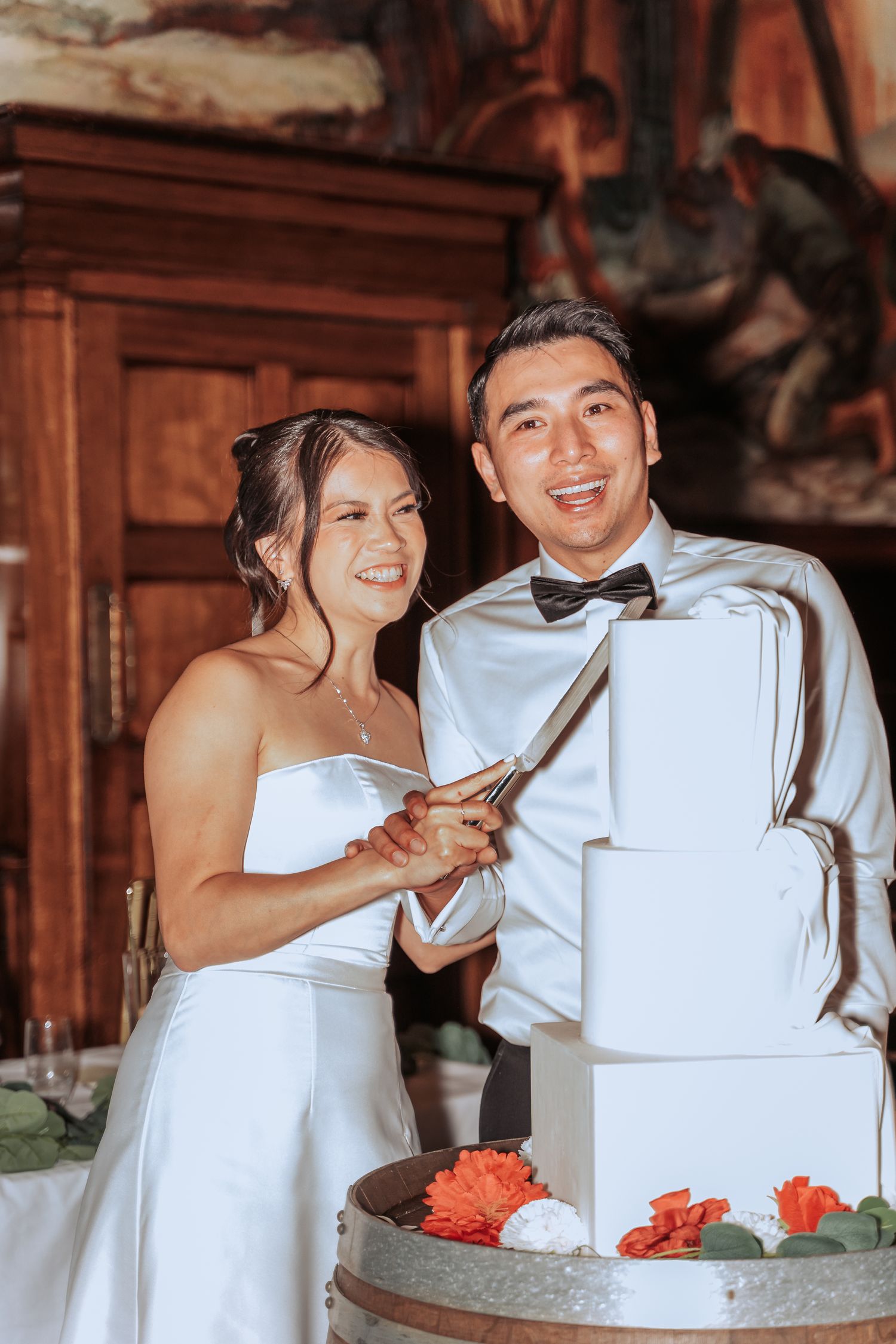 A couple cuts their white tiered wedding cake together at their reception.