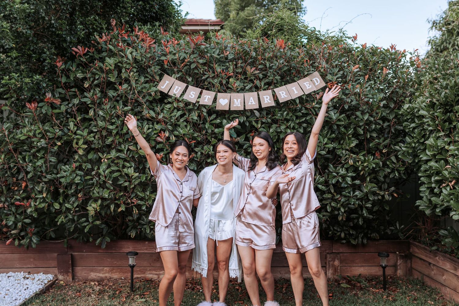 Four people in matching silk robes pose with a banner against a flowering hedge.