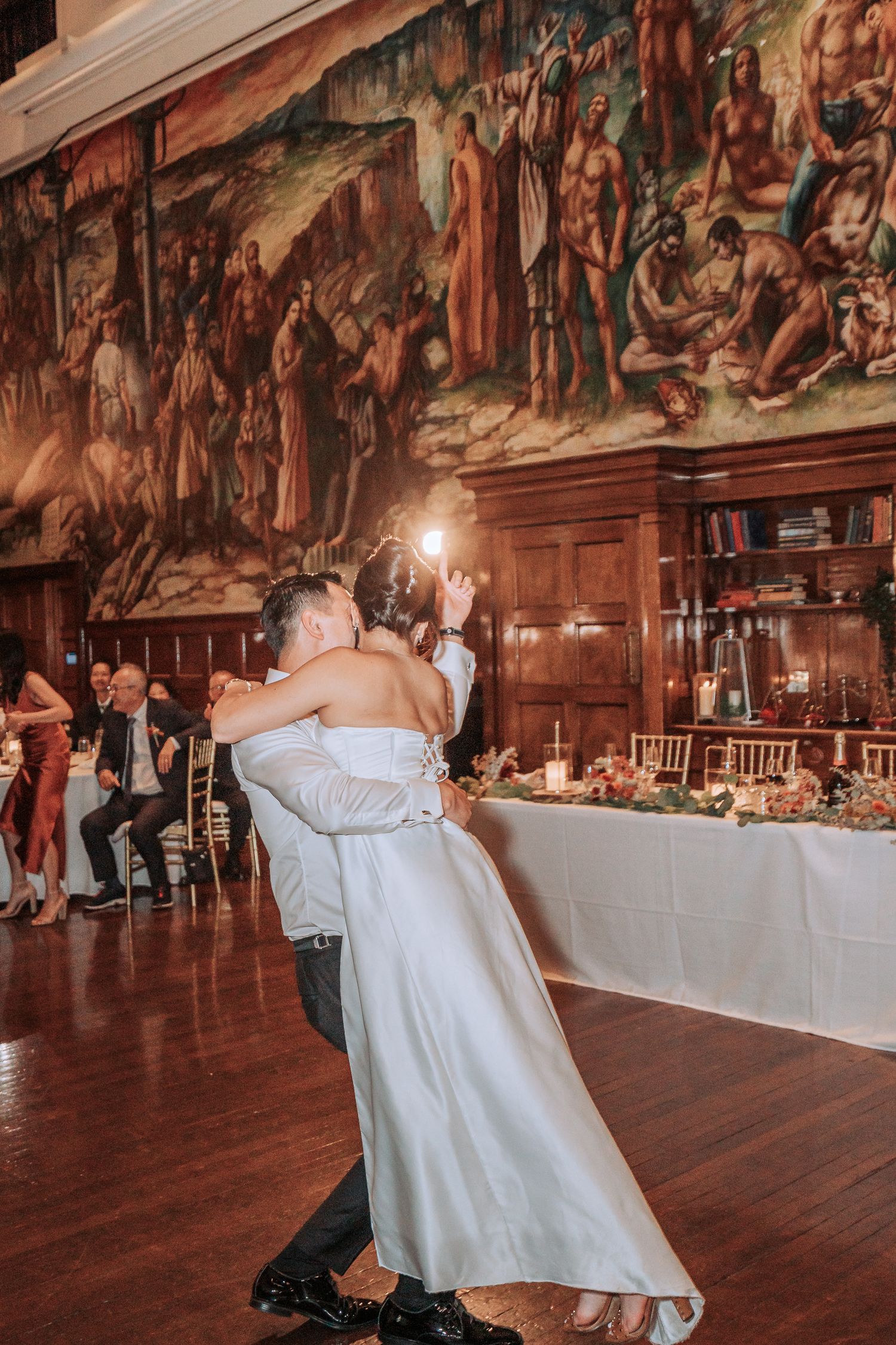 A couple shares their first dance beneath Renaissance murals at wedding reception.