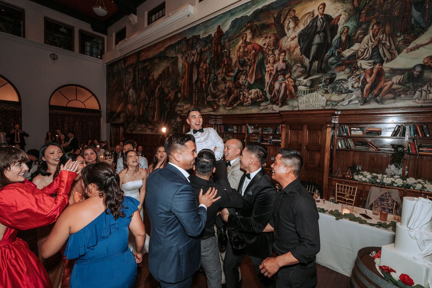 Wedding reception guests socialize under large Renaissance-style murals.
