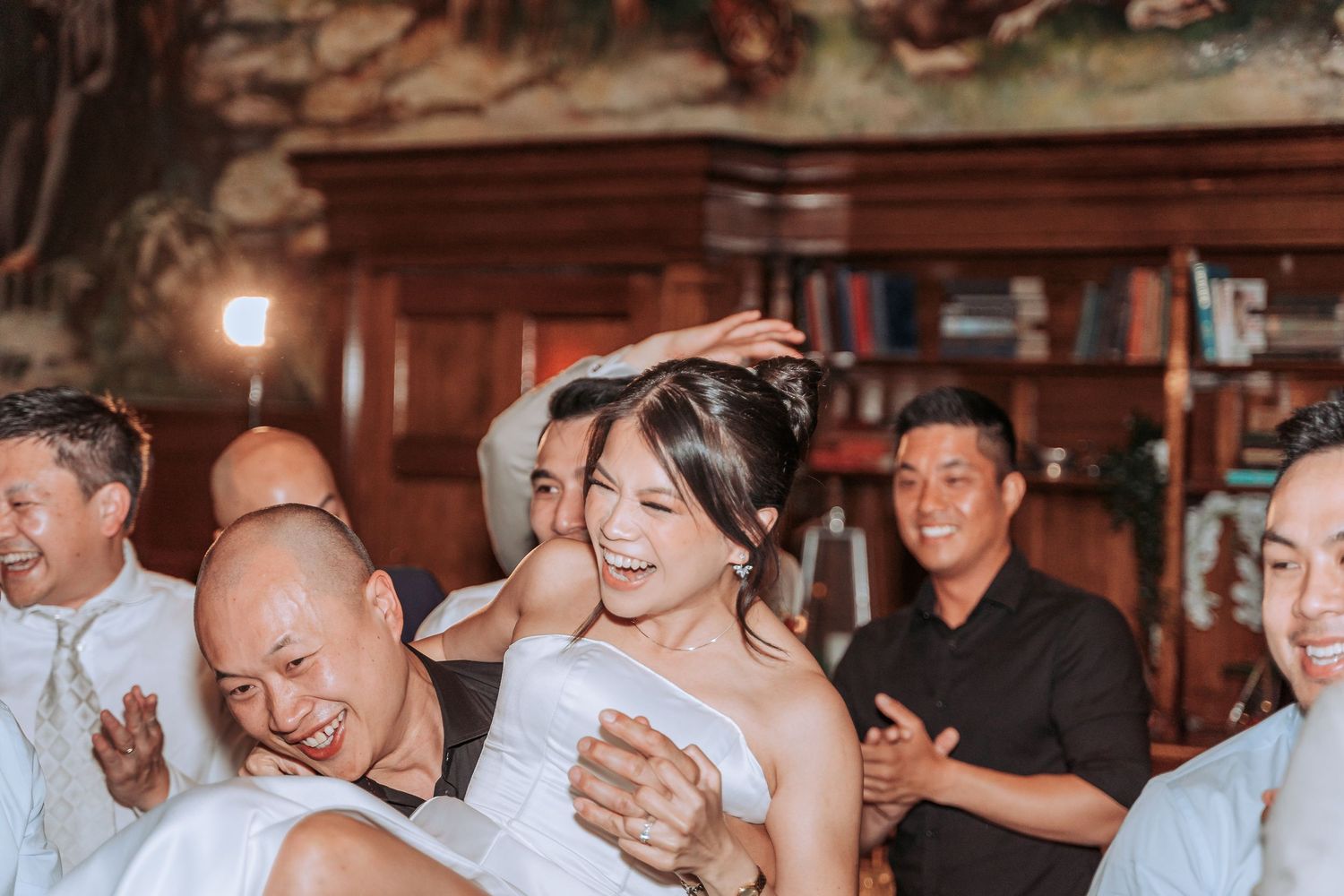 Wedding reception guests dancing and celebrating in a room with wooden wall panels.