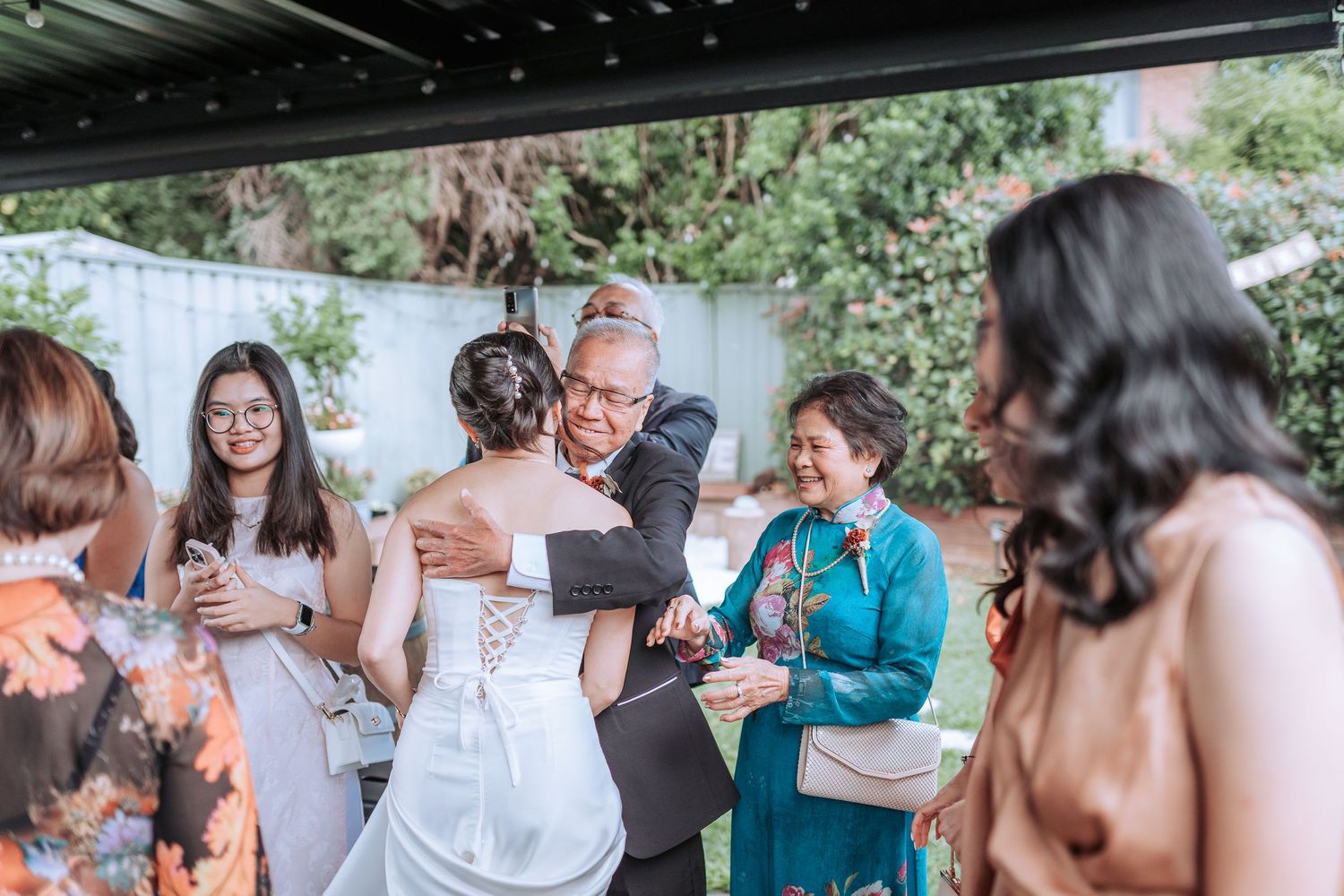 Wedding guests gather around to celebrate during an outdoor reception.