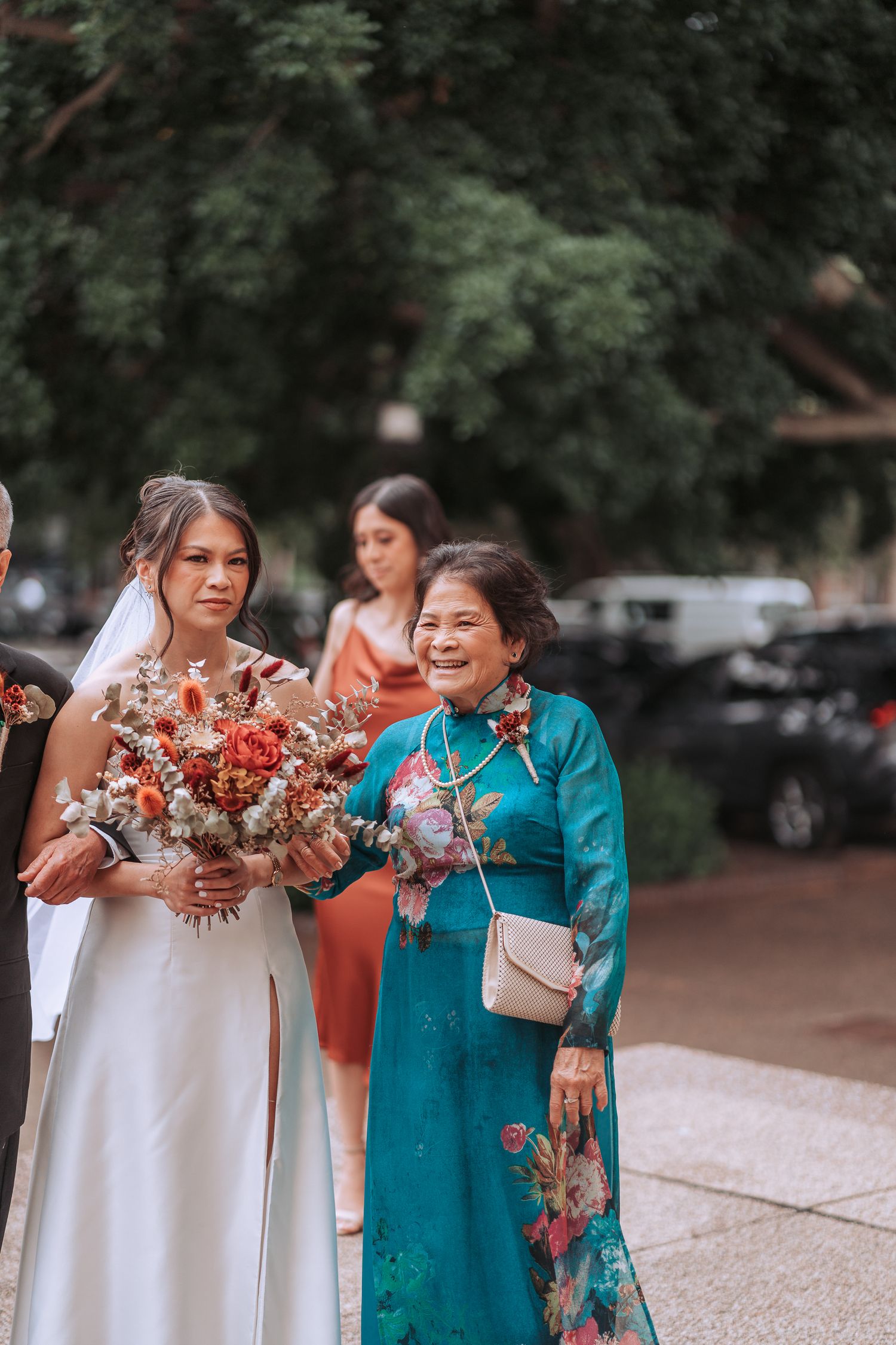 A bride in white holds a vibrant red bouquet while standing with family members in traditional attire.