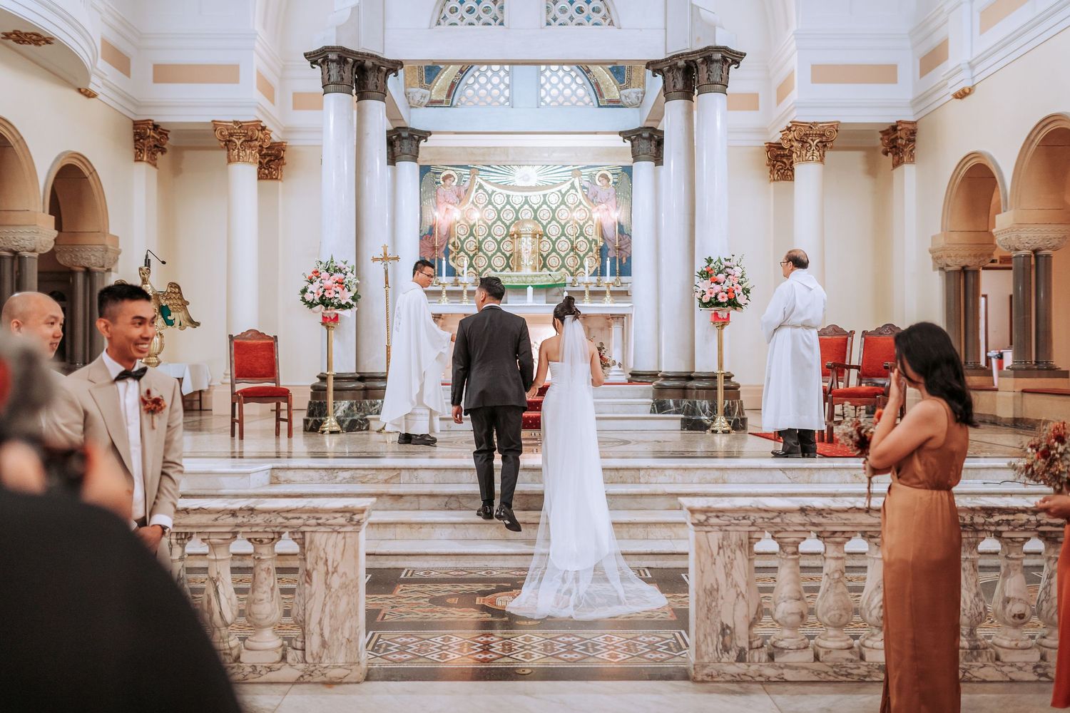 A couple stands at the altar of an ornate Catholic church during their wedding ceremony.