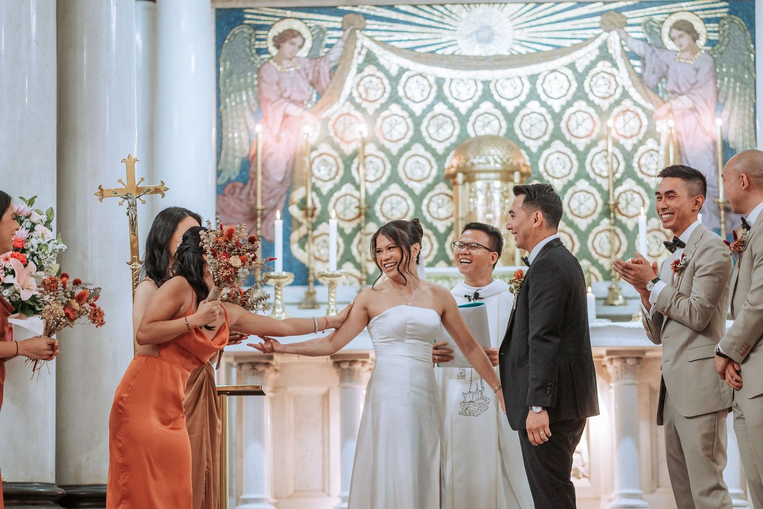 Wedding ceremony in progress inside a beautifully decorated church with pink floral arrangements.