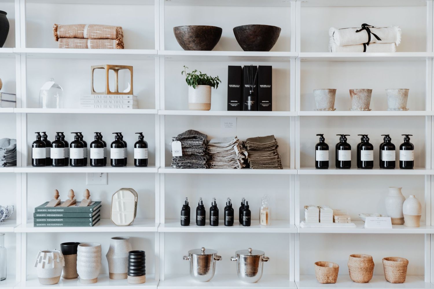 Retail shelves displaying neatly organized bottles, ceramics, and products in a modern minimalist shop interior.