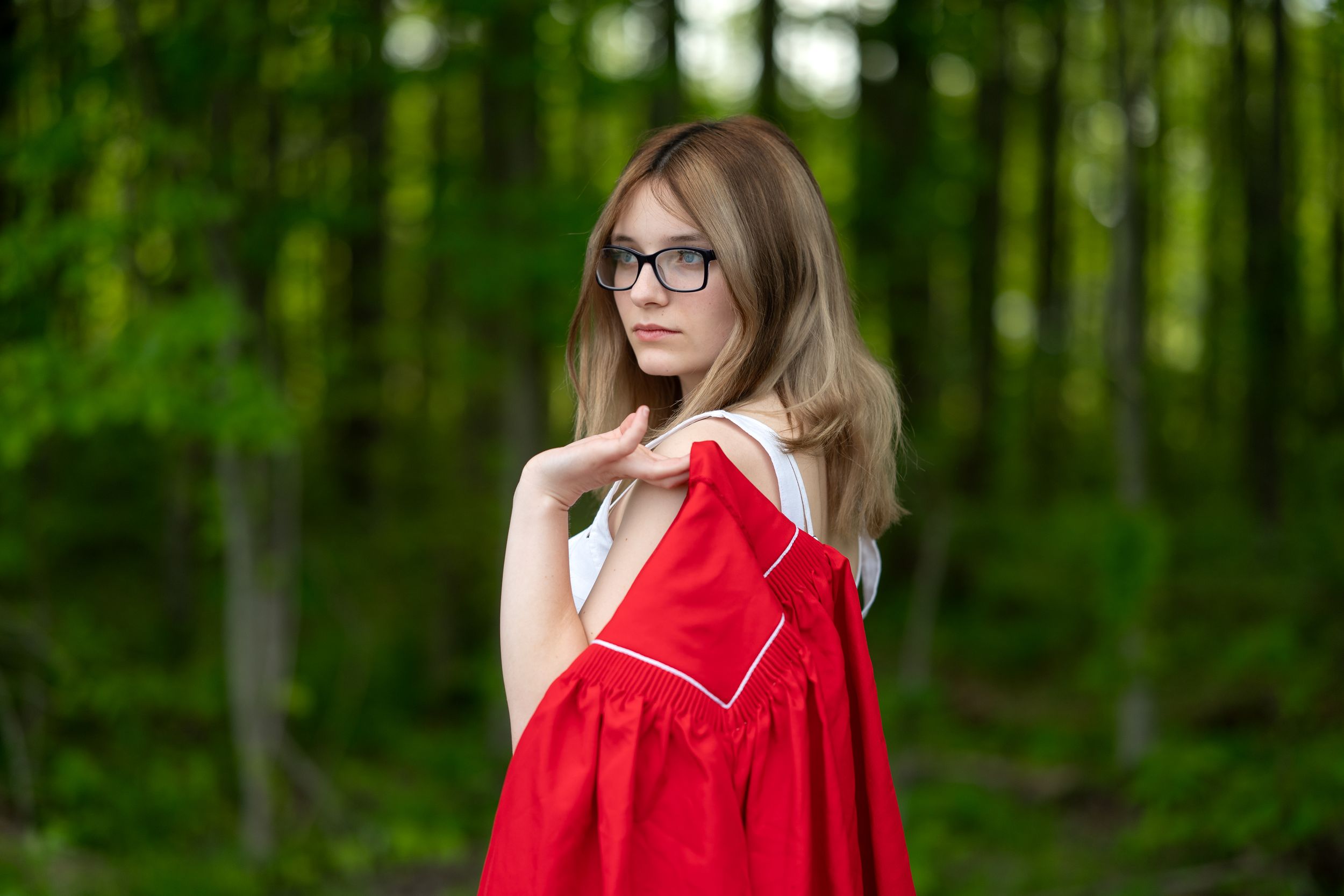 A woman in a bright red jacket poses thoughtfully in a lush green forest setting.