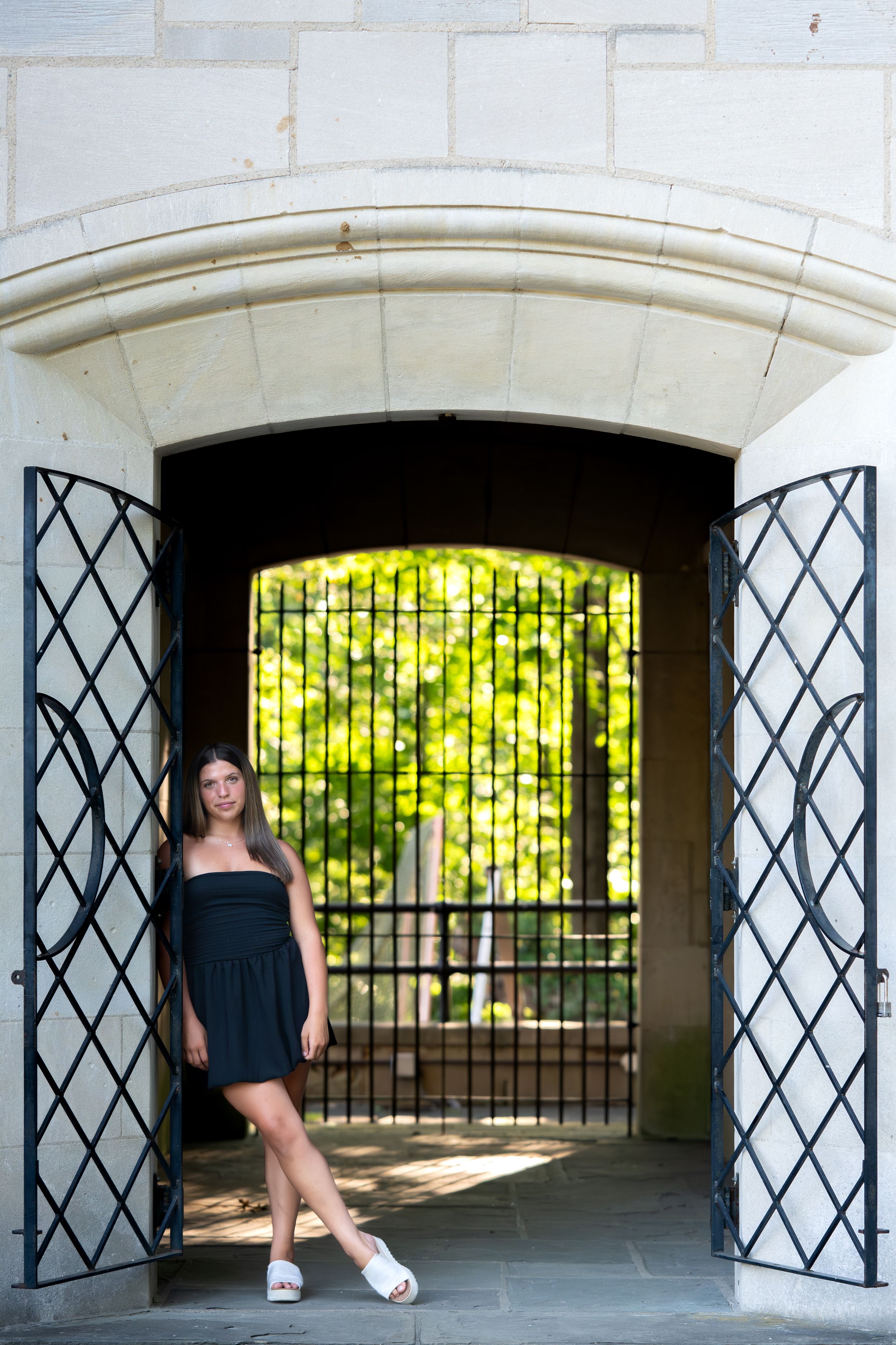 A sequence showing different poses taken in an elegant stone archway with decorative metal gates and green foliage beyond.
