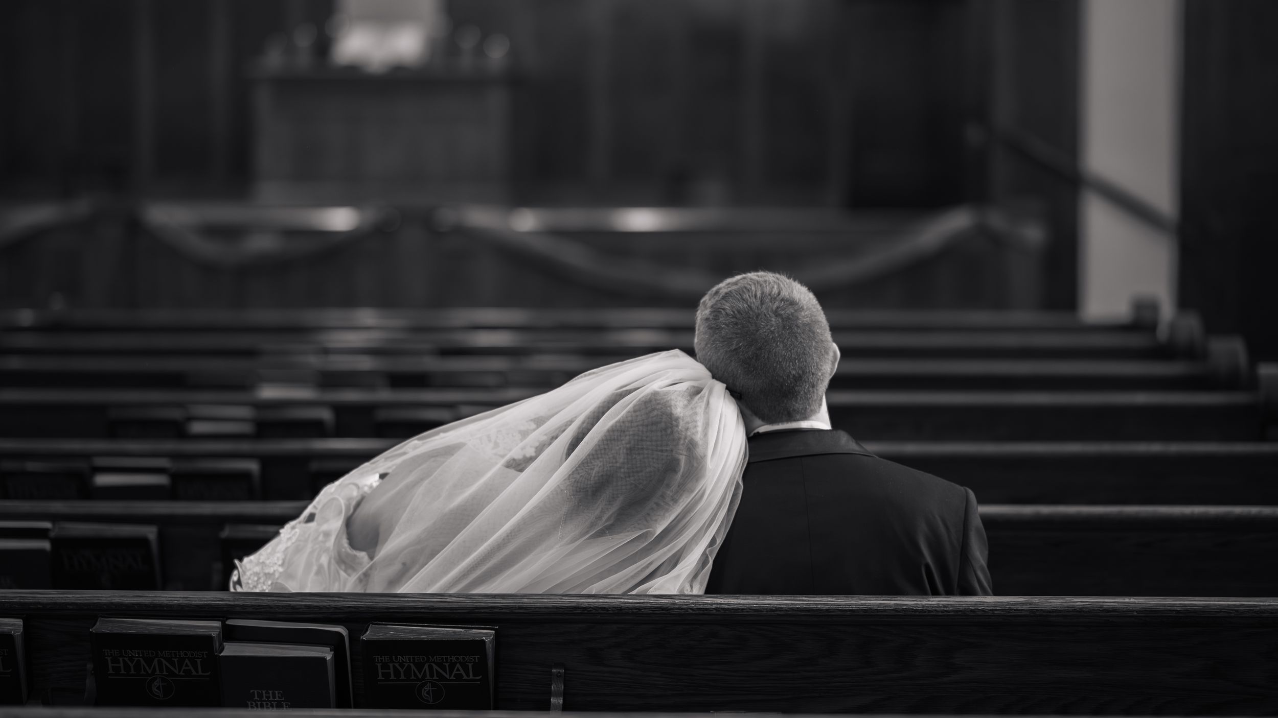 Black and white photo of a bride and groom sitting together in church pews on their wedding day.