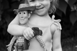 A young child holds a Woody doll from Toy Story in a sweet black and white portrait.