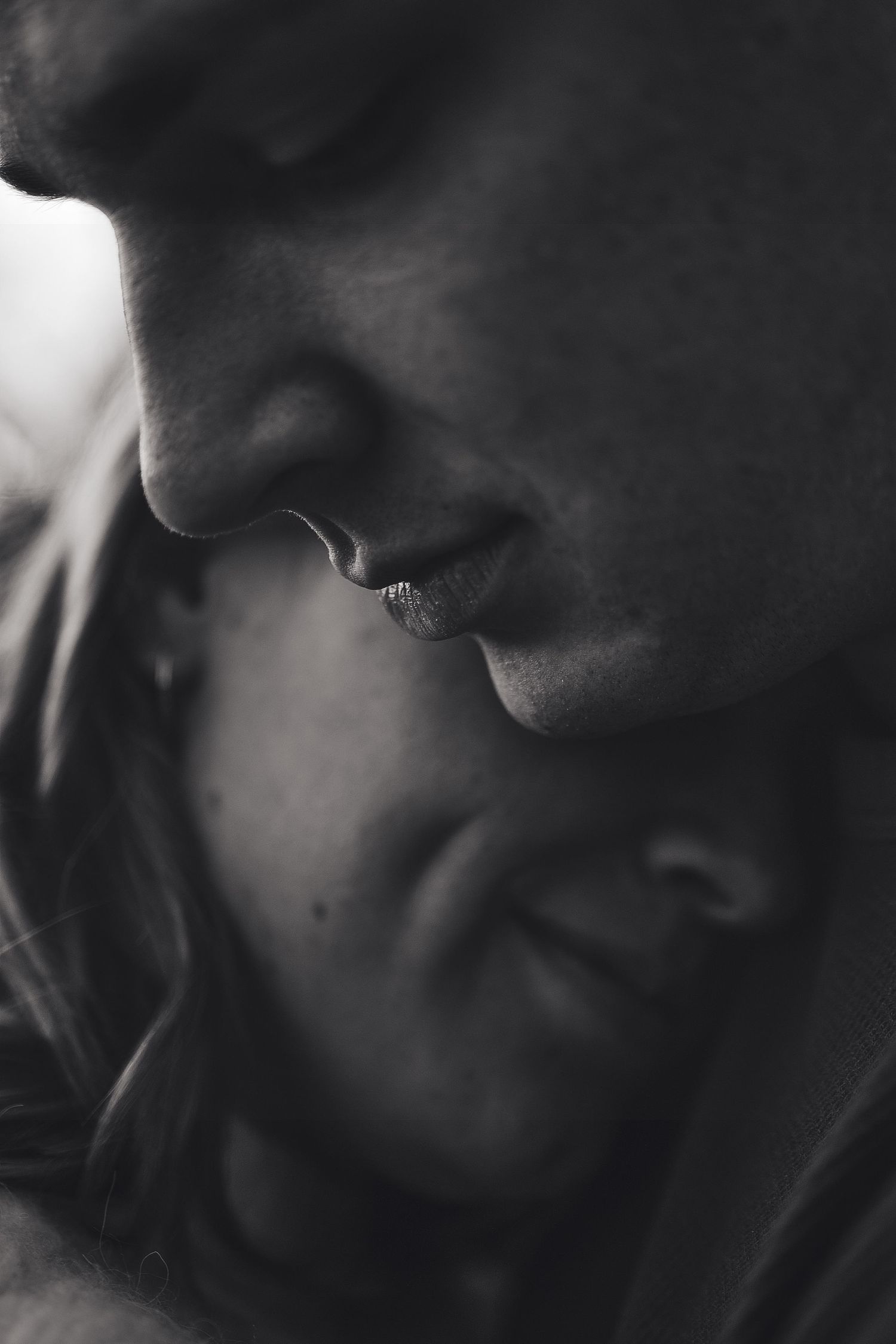 Black and white close-up of a couple embracing, the woman resting her head against the man’s chest with a tender expression.