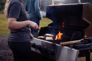 Someone grilling food on a gas barbecue with flames visible in the evening light.