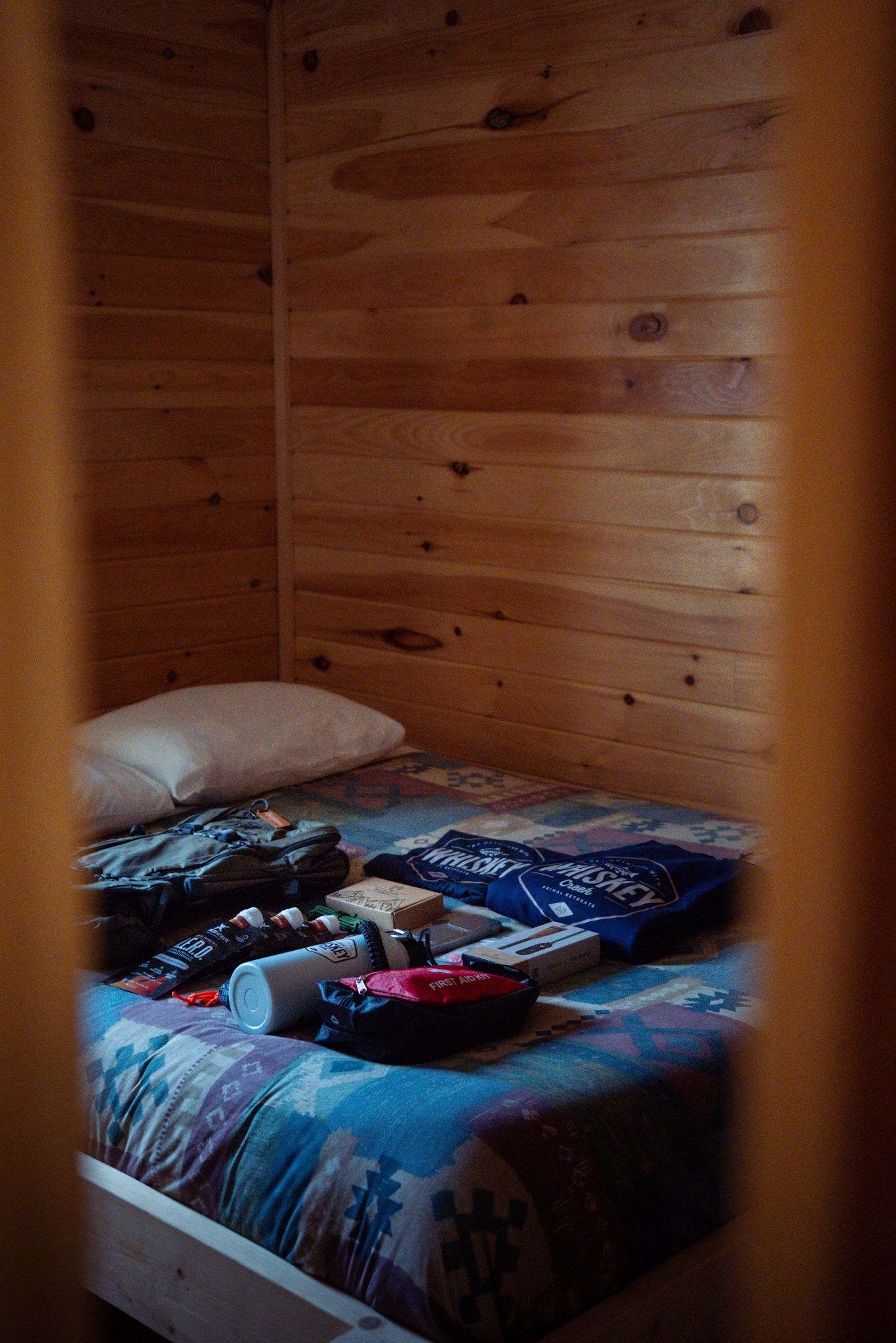 Interior view of wooden cabin bedroom with folded clothes on a blue patterned bed through a doorframe.