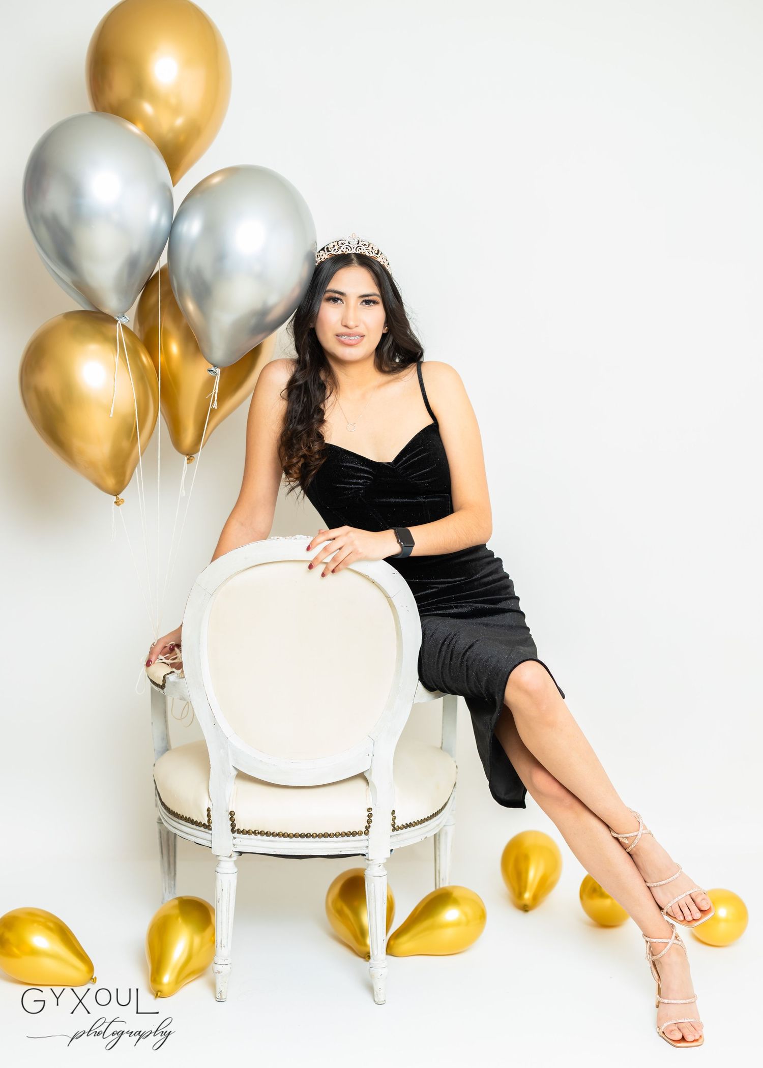 Sophisticated portrait on white chair with metallic balloons in background.