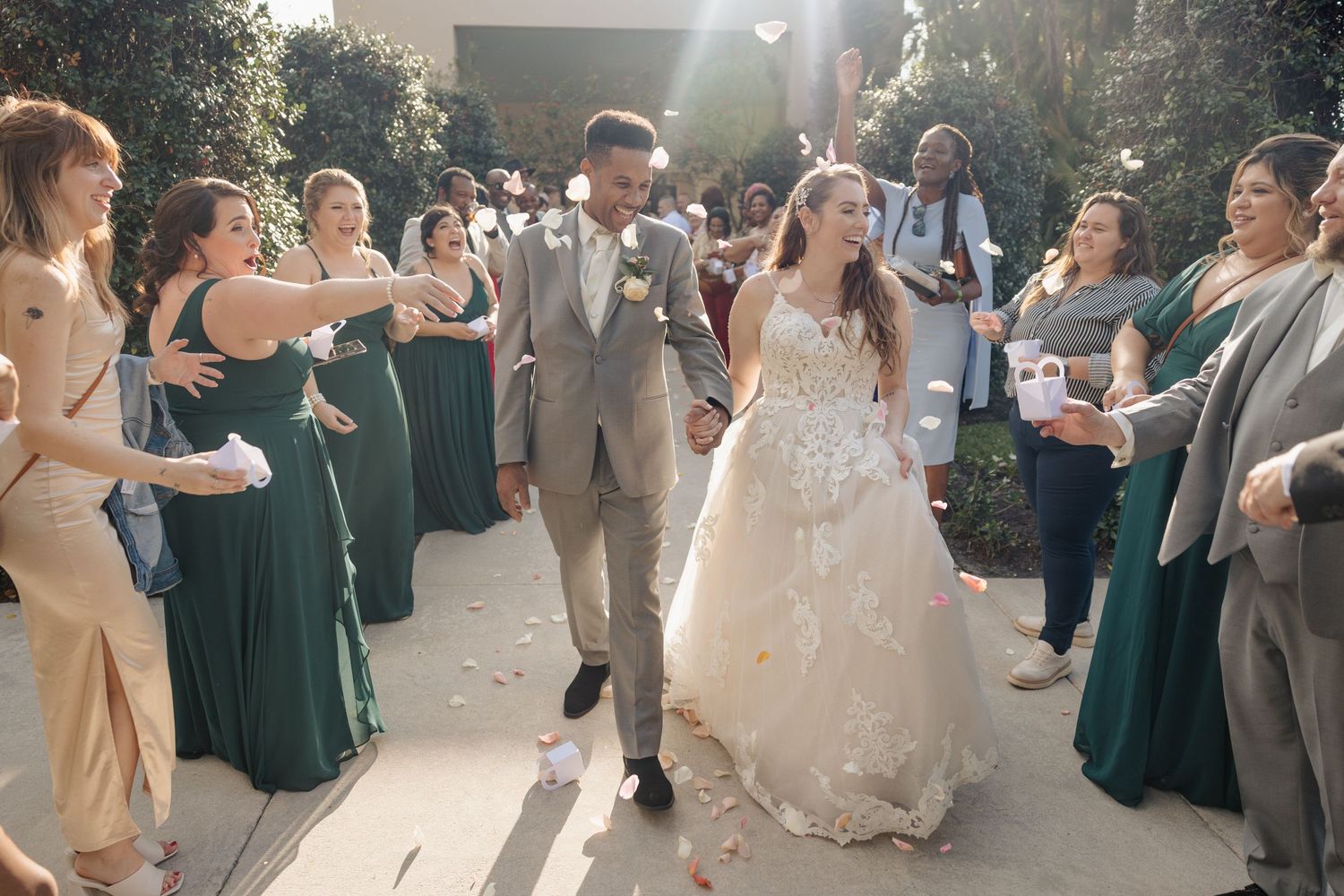 Wedding guests in green dresses line a pathway to celebrate the newlyweds.