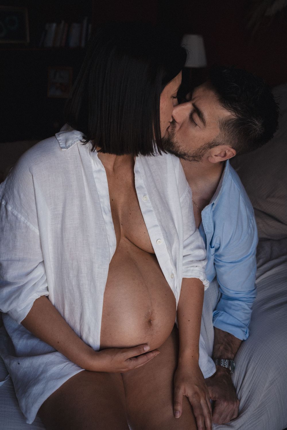 Intimate moment between couple in white and blue shirts embracing in dim lighting.