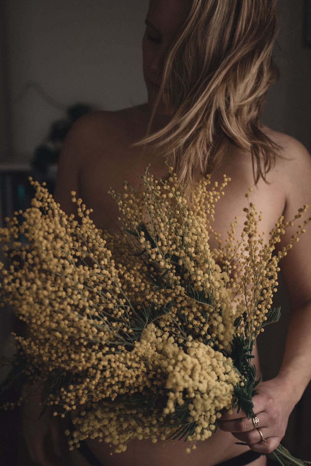 Femme enceinte tenant des fleurs de mimosa jaunes sur une photo boudoir artistique.