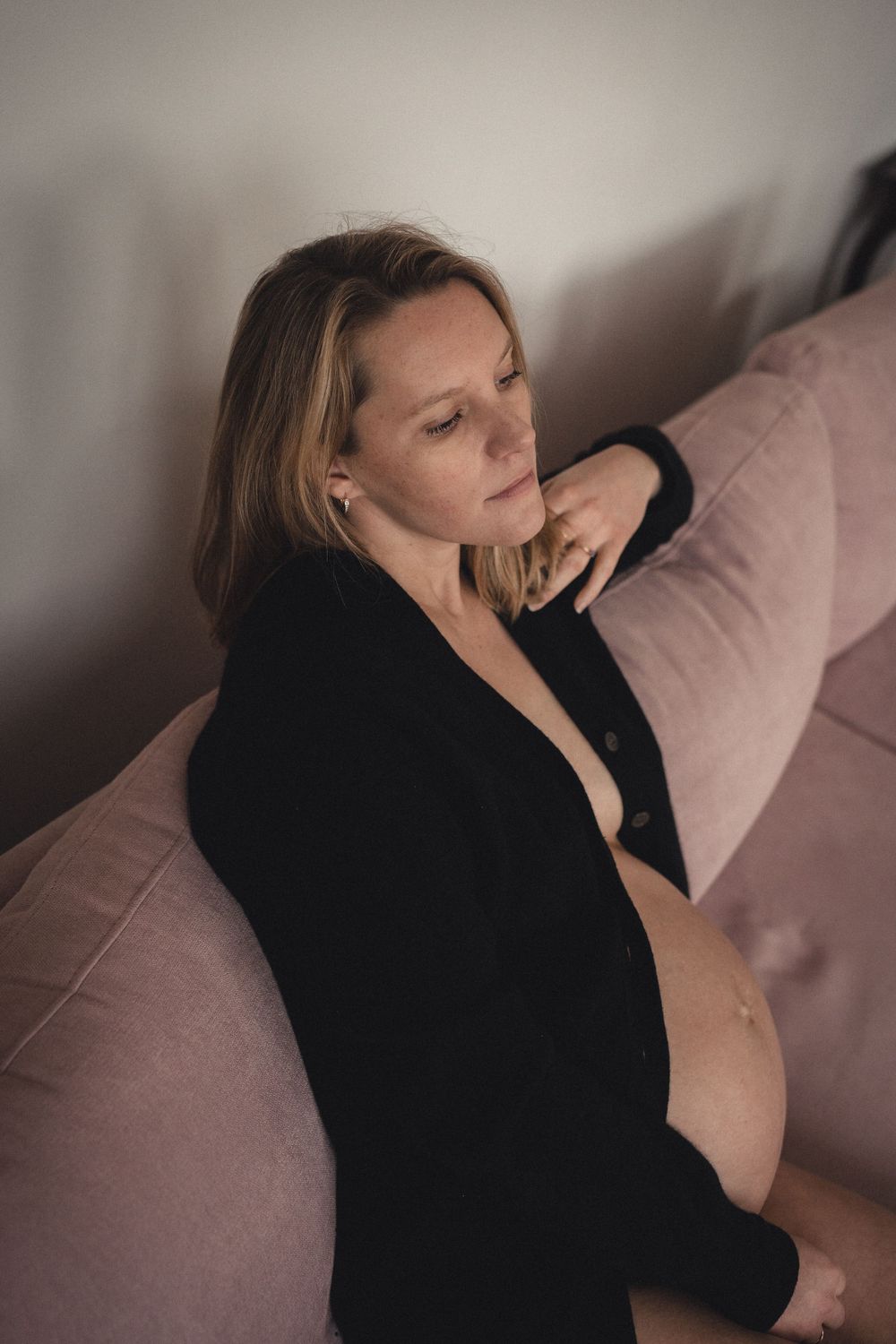 Artistic maternity portrait showing an expectant mother resting on a pink couch.