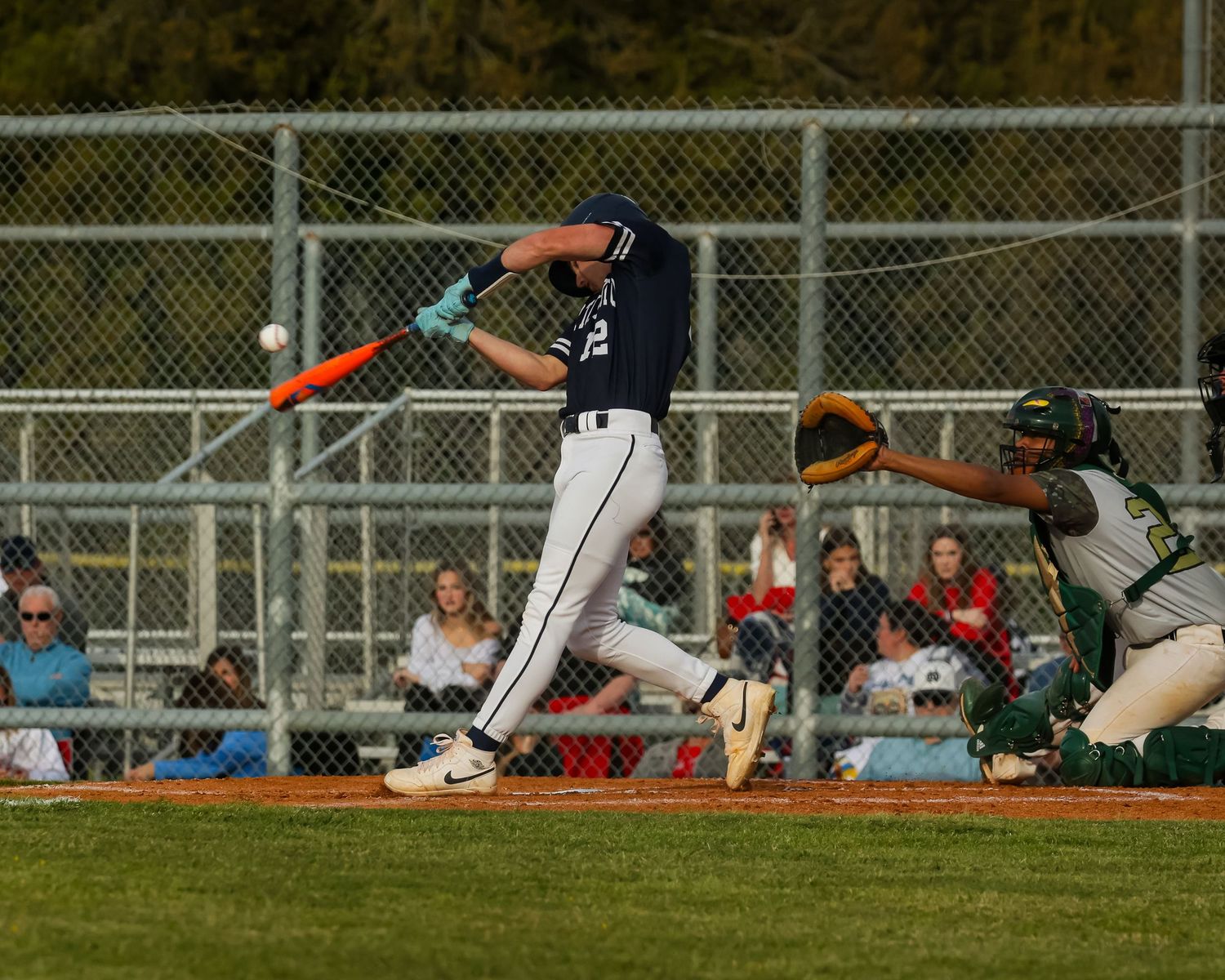 Baseball batter in navy uniform swings at pitch during game while catcher awaits in crouch position behind home plate.