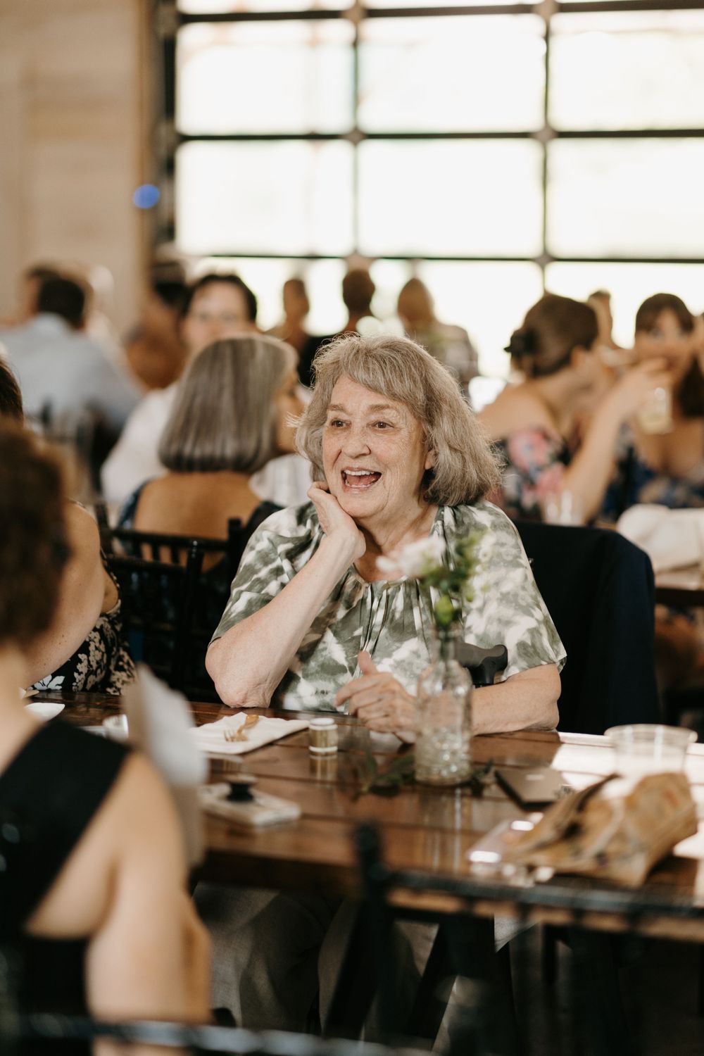 Elderly woman smiles joyfully at wedding reception dinner table.