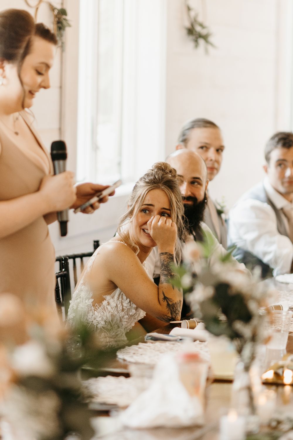 Smiling bride rests chin on hand listening to speech at wedding reception.