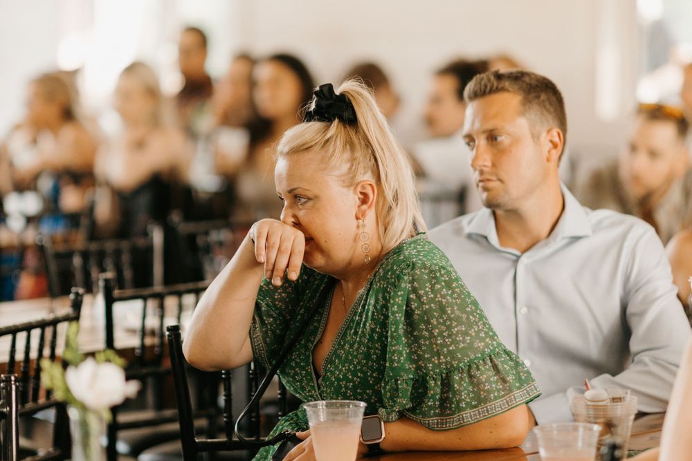 Emotional wedding guest in green dress wipes tears during reception speech.