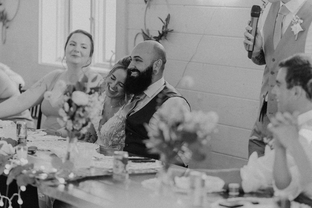 Black and white photo of bride and groom laughing during wedding speeches.