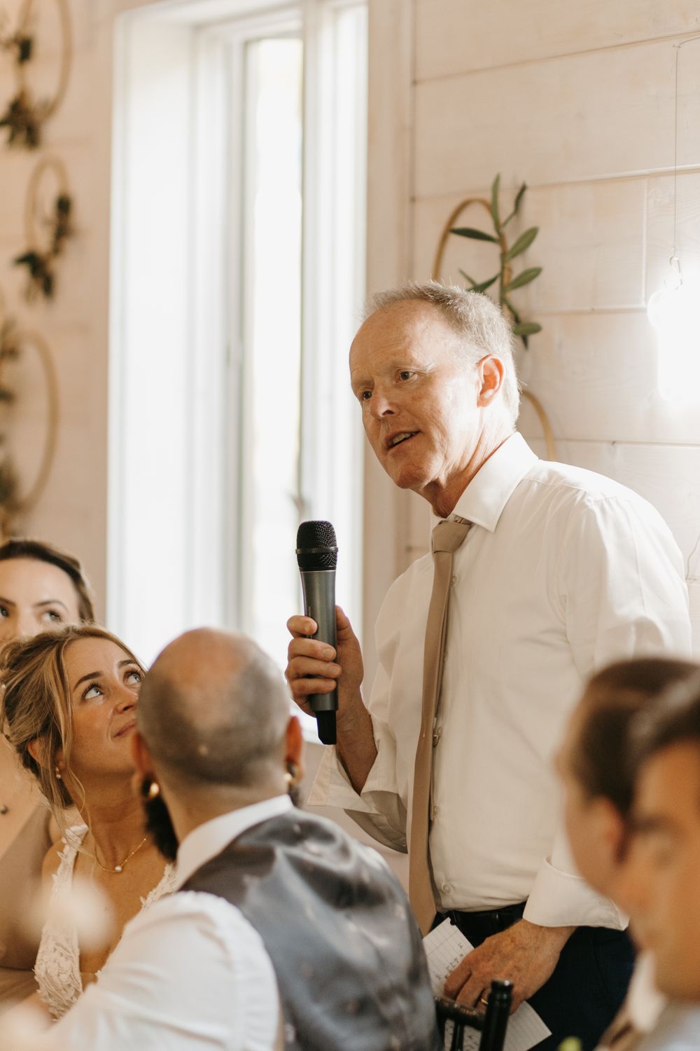 Older man delivers emotional wedding speech with microphone at elegant reception.