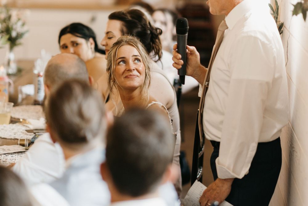 A bride gazes up adoringly during wedding reception speeches at an elegant venue.