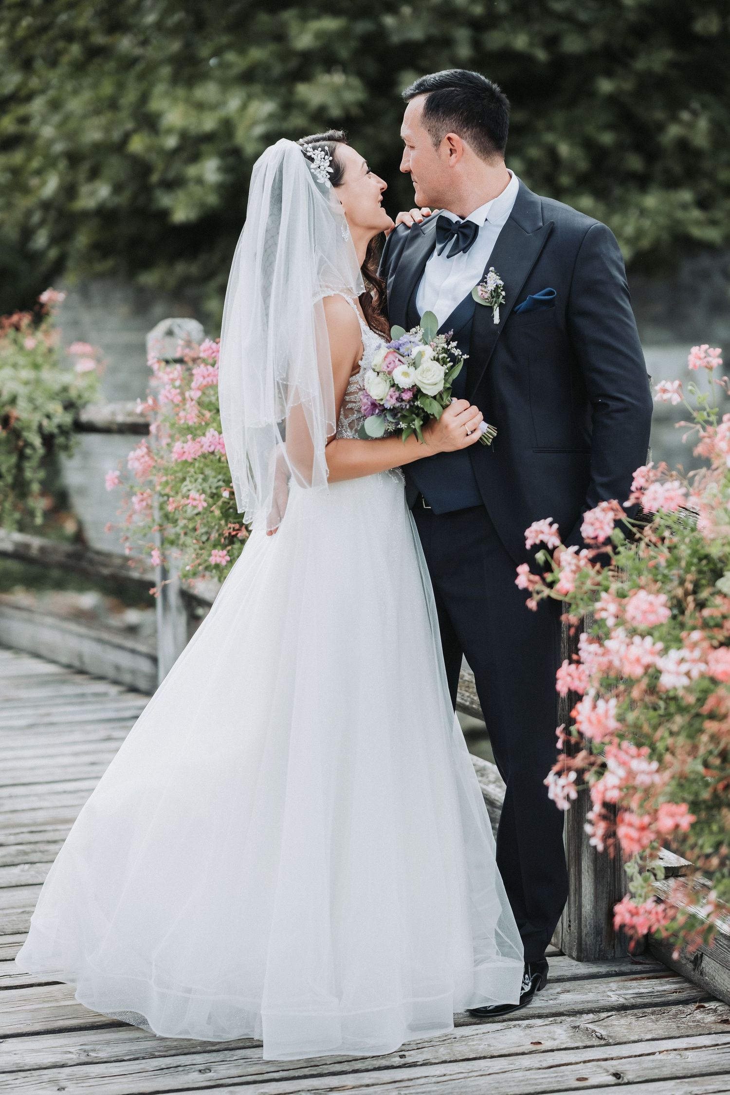 Romantic wedding portrait of couple embracing in garden with white floral backdrop.