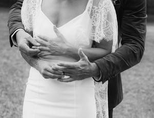 Black and white photo of groom embracing bride in lace wedding gown from behind.