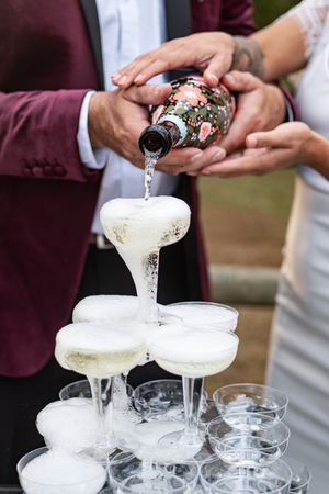 Champagne tower being filled with sparkling wine at outdoor wedding reception celebration.
