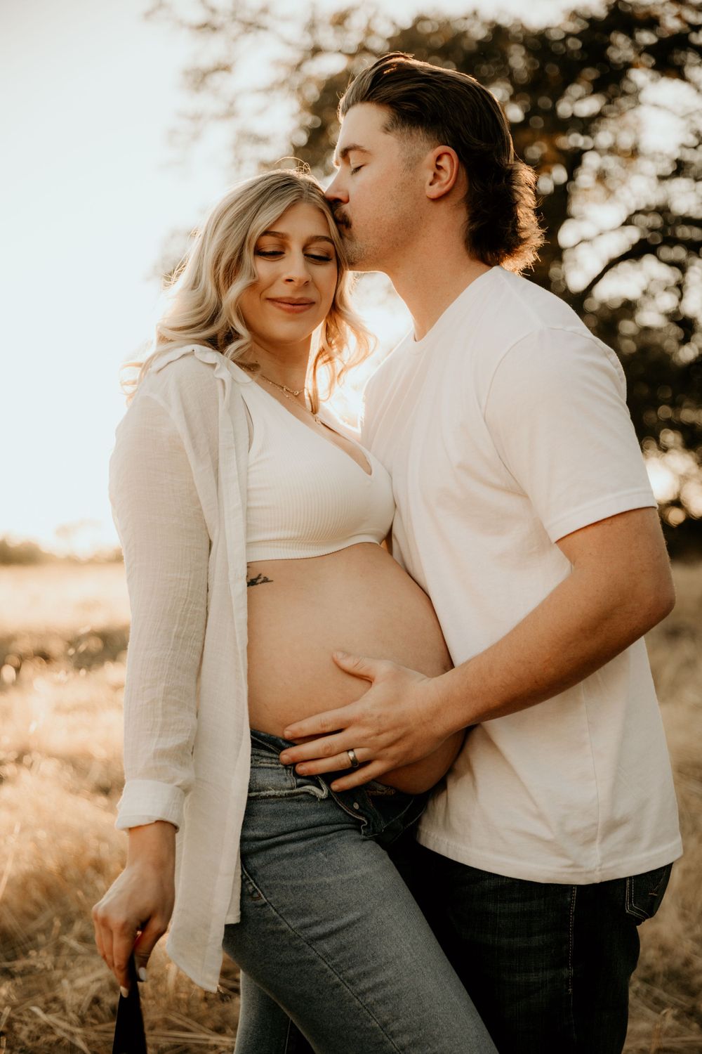 Warm sunset maternity session showing loving couple embracing in outdoor setting.