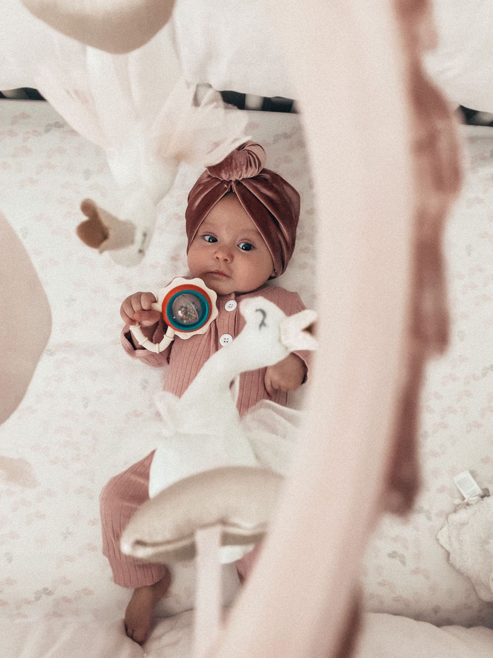 A baby in white outfit and brown turban holds a rattle while surrounded by floating fabric.