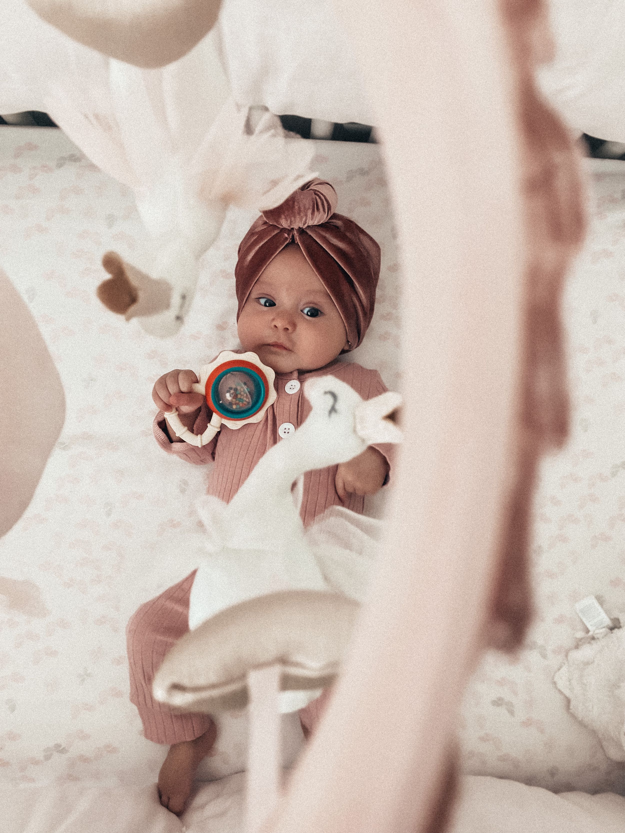 A baby in white outfit and brown turban holds a rattle while surrounded by floating fabric.