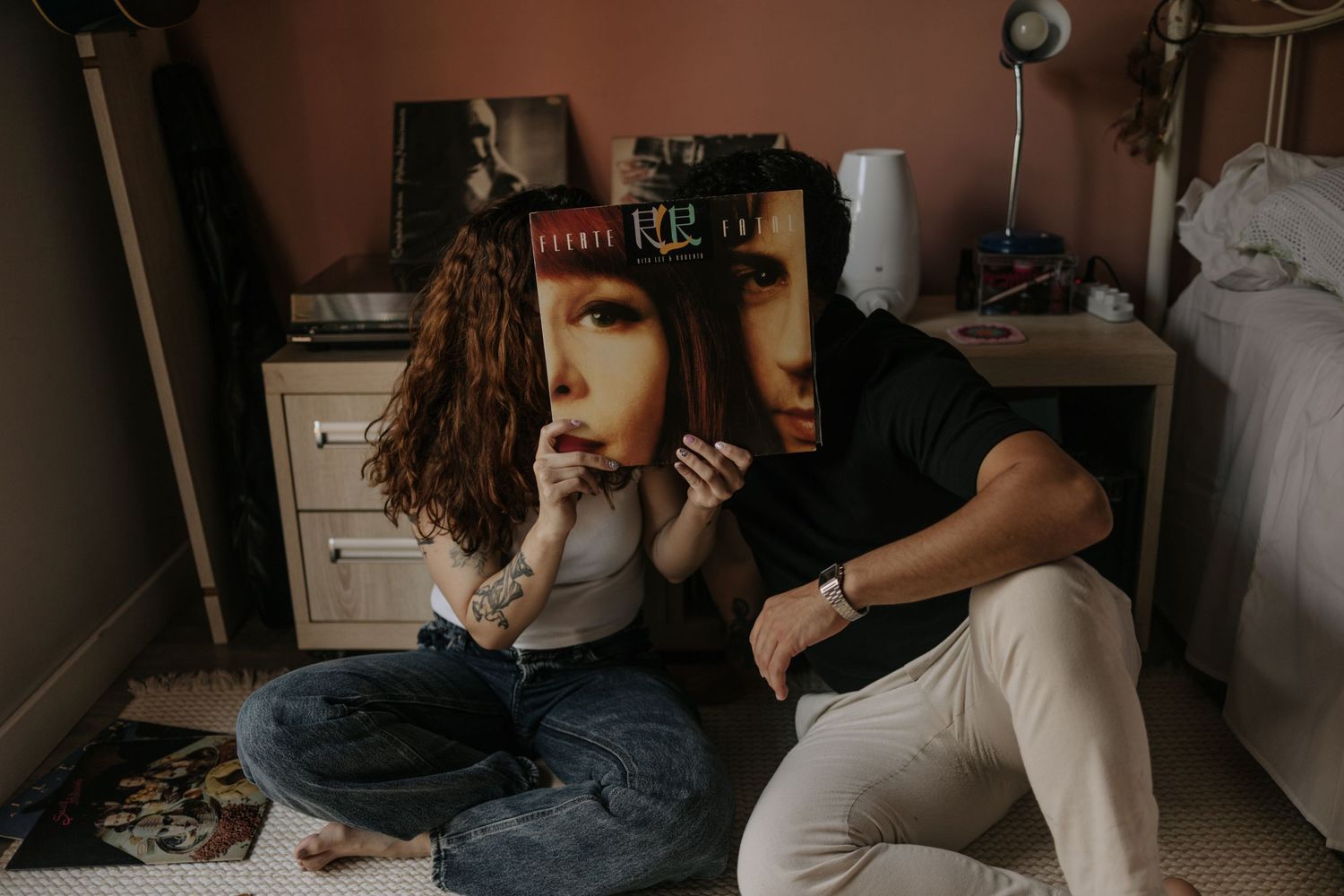 Couple in their bedroom, sitting on the floor hiding their faces behing a vinyl