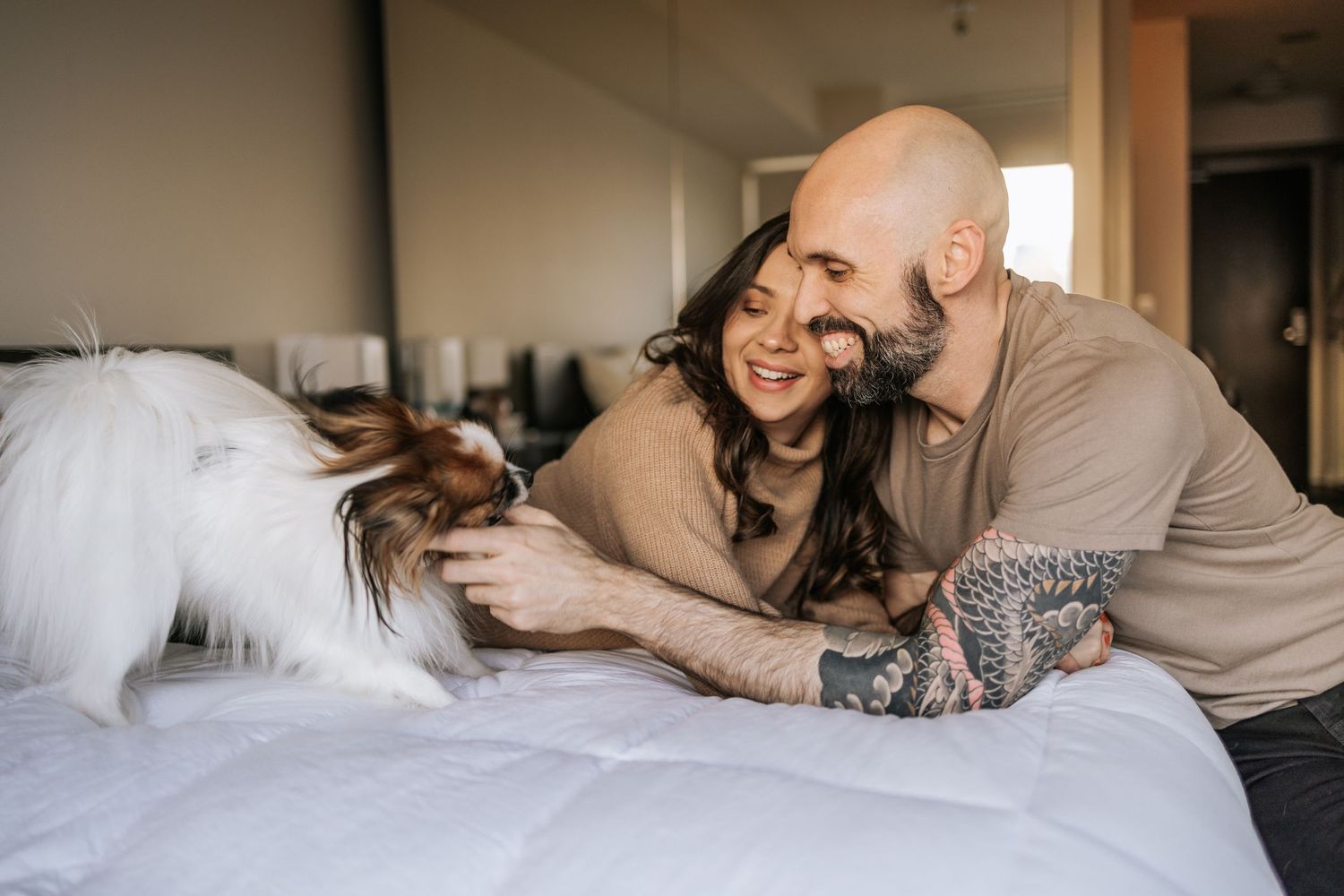 Couple in their bedroom playing with their little dog on their bed